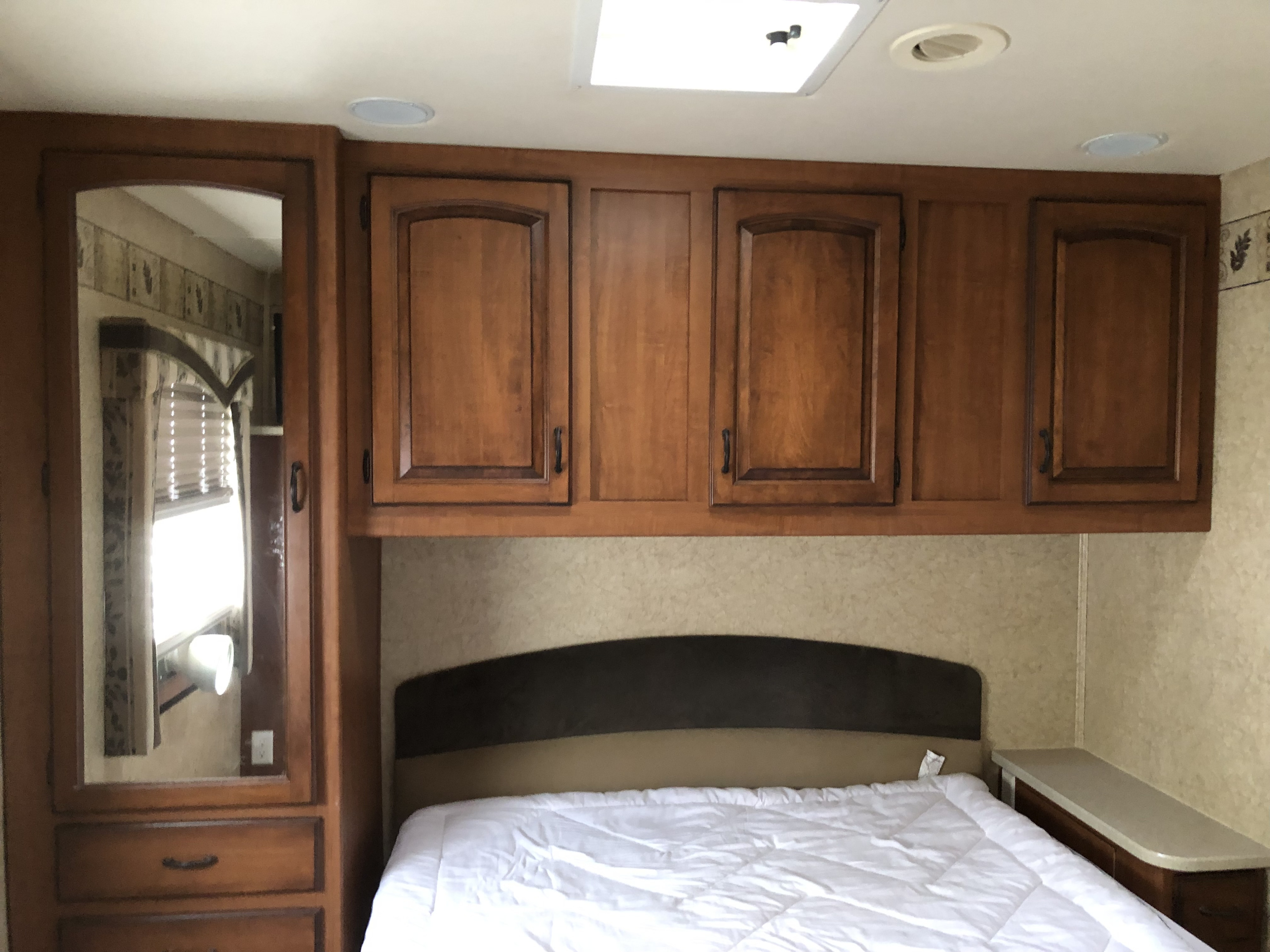 Cozy RV rental bedroom interior with a bed, wooden overhead cabinets, and a wardrobe with a mirror reflecting a window.. Jayco Greyhawk 2008