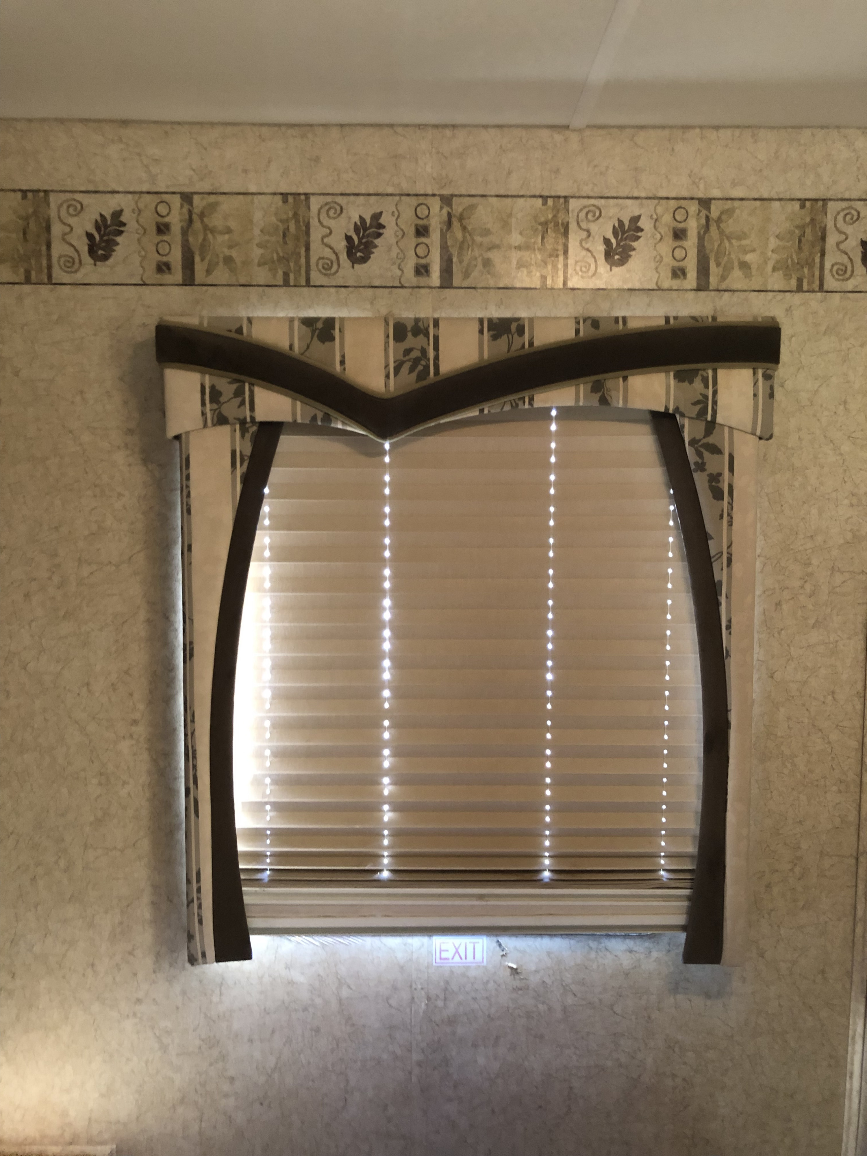 RV rental interior: A window with light-filtering blinds, decorative valance, and a small 'EXIT' sign below, set against patterned wallpaper.. Jayco Greyhawk 2008