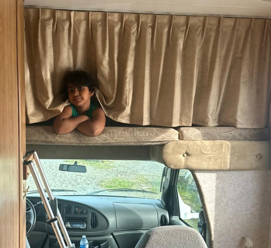 Young child peeks from an RV rental's cab-over bunk, arms crossed. Crutches lean by the driver's seat. Ready for travel!. Adventurer Adventurer Motorhome 2007
