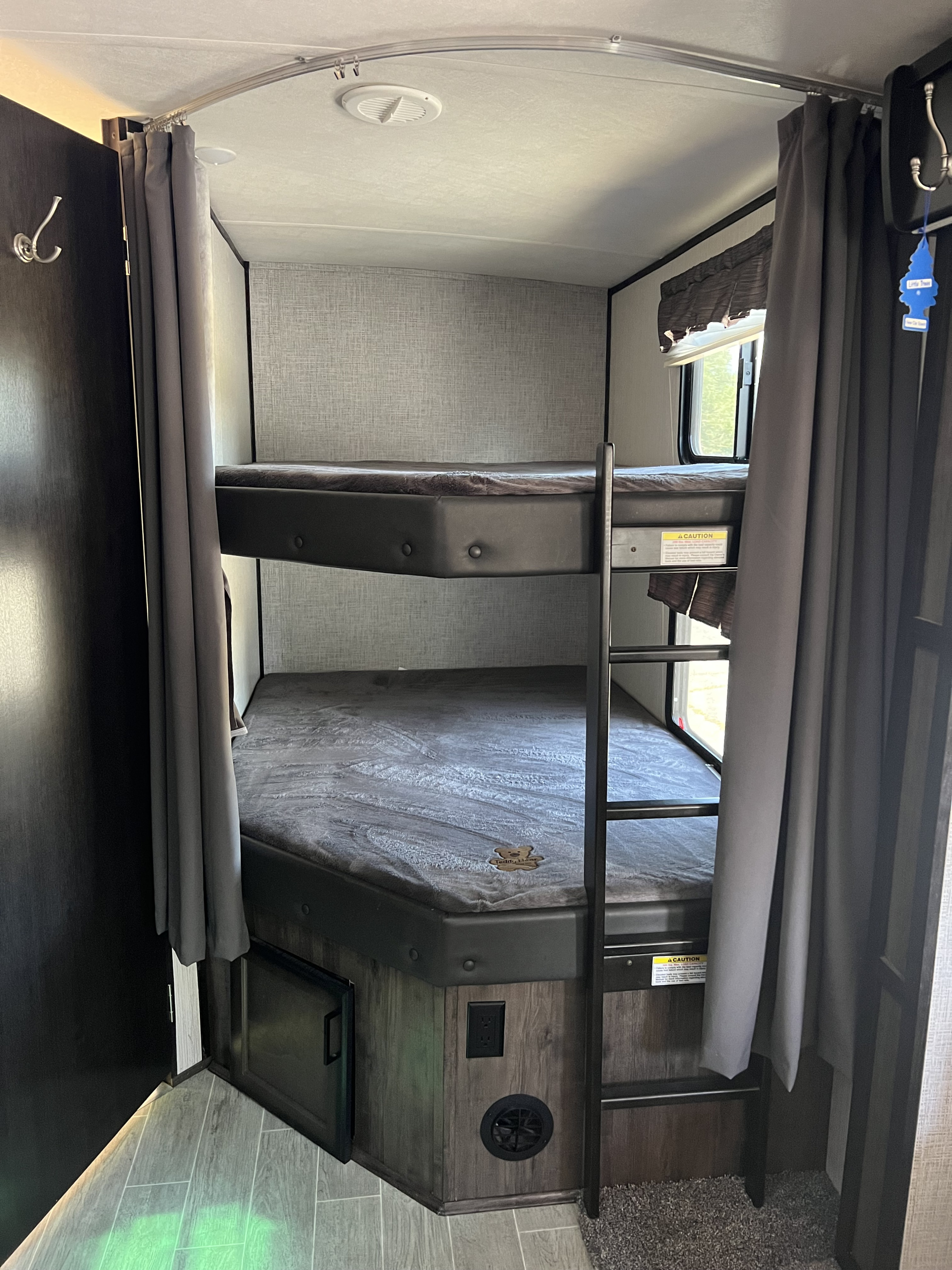 Two cozy bunk beds in an RV rental, complete with privacy curtains, a ladder, and a window, ideal for resting.. Heartland RVs Mallard 2020