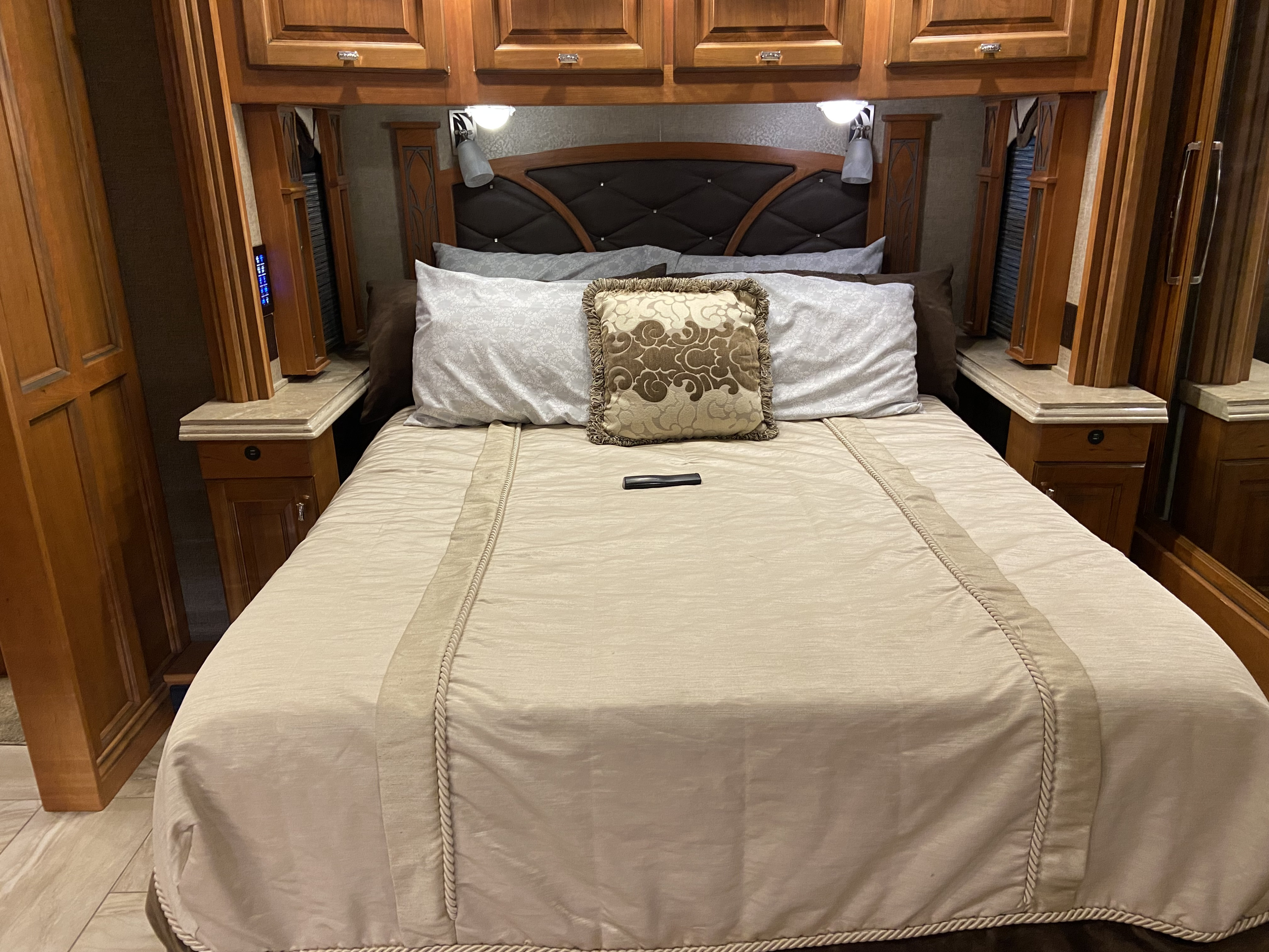Spacious RV rental bedroom featuring a full bed with decorative pillows, built-in wooden cabinetry, and bedside lamps.. Tiffin Motorhomes Allegro Bus 2017