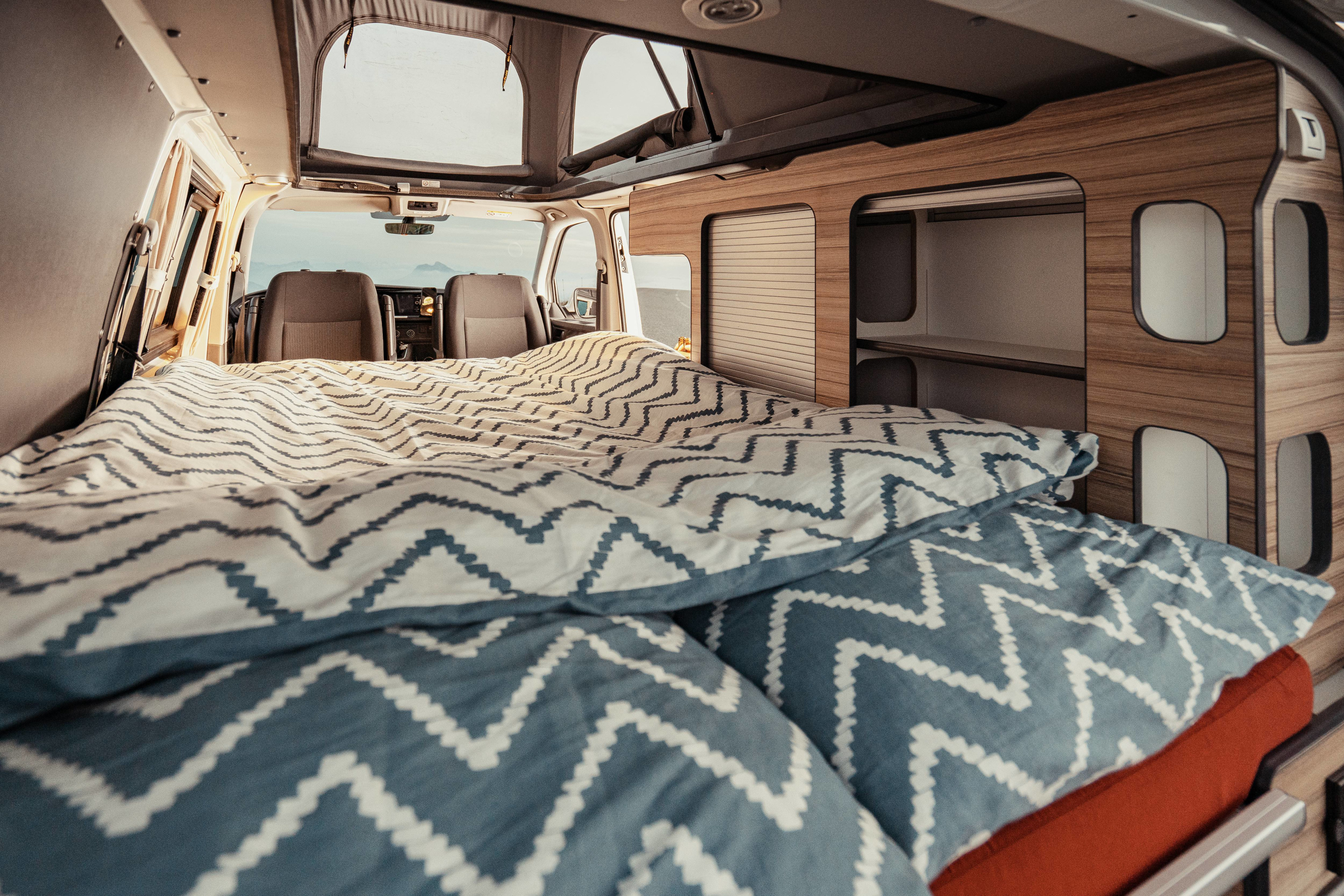 Cozy RV rental interior with bed, built-in cabinets, and a scenic view from the front seats. Perfect for a road trip adventure.. Volkswagen Transporter T6.1 2022