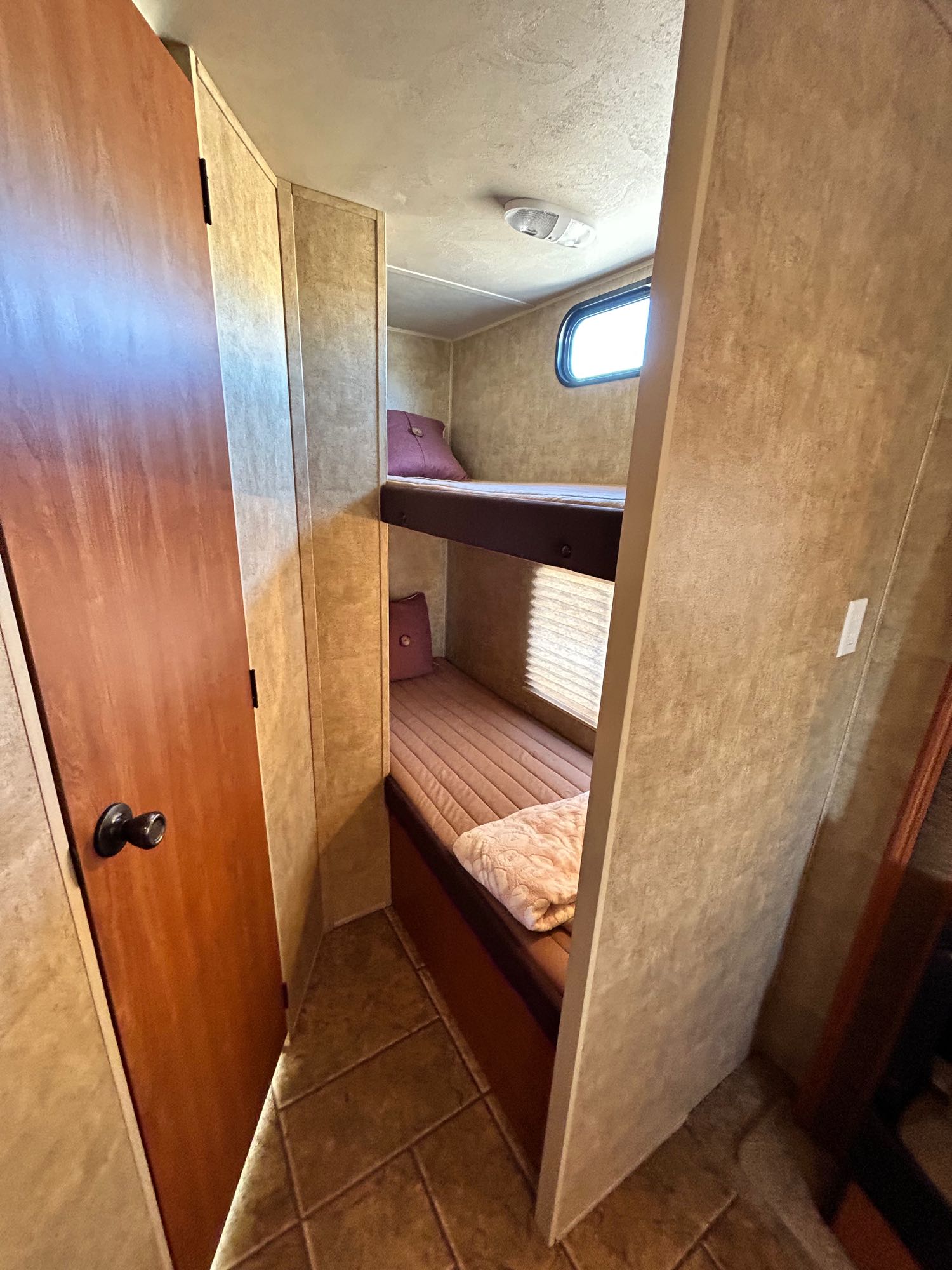 RV rental interior showcasing cozy bunk beds, a small window, and a brown door on the left leading to another section.. Forest River Cherokee 2013