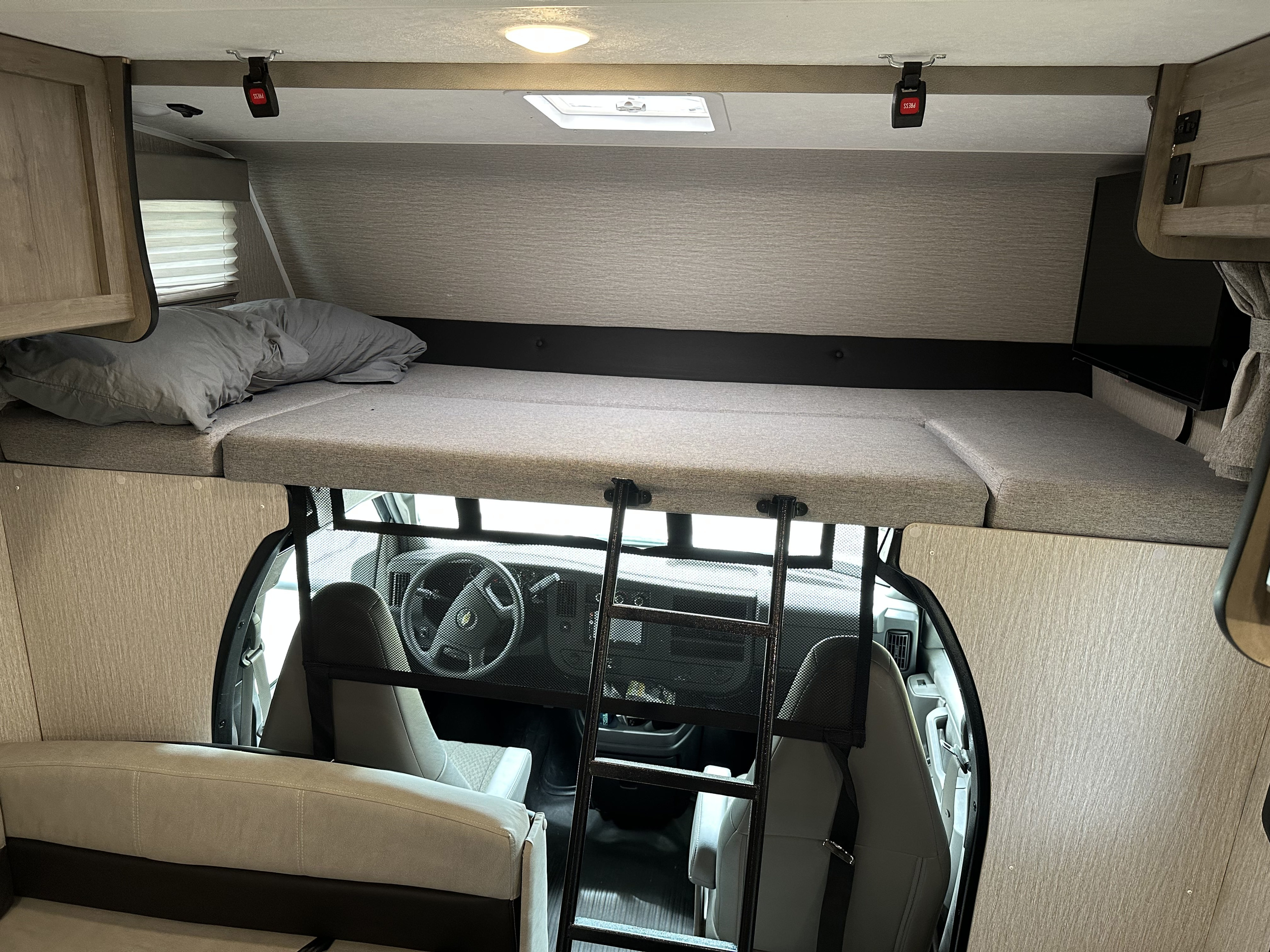 Inside an RV rental: the forward cab-over bunk with bedding, ladder, safety net, and view down to the driver's cockpit.. Coachmen Other 2022
