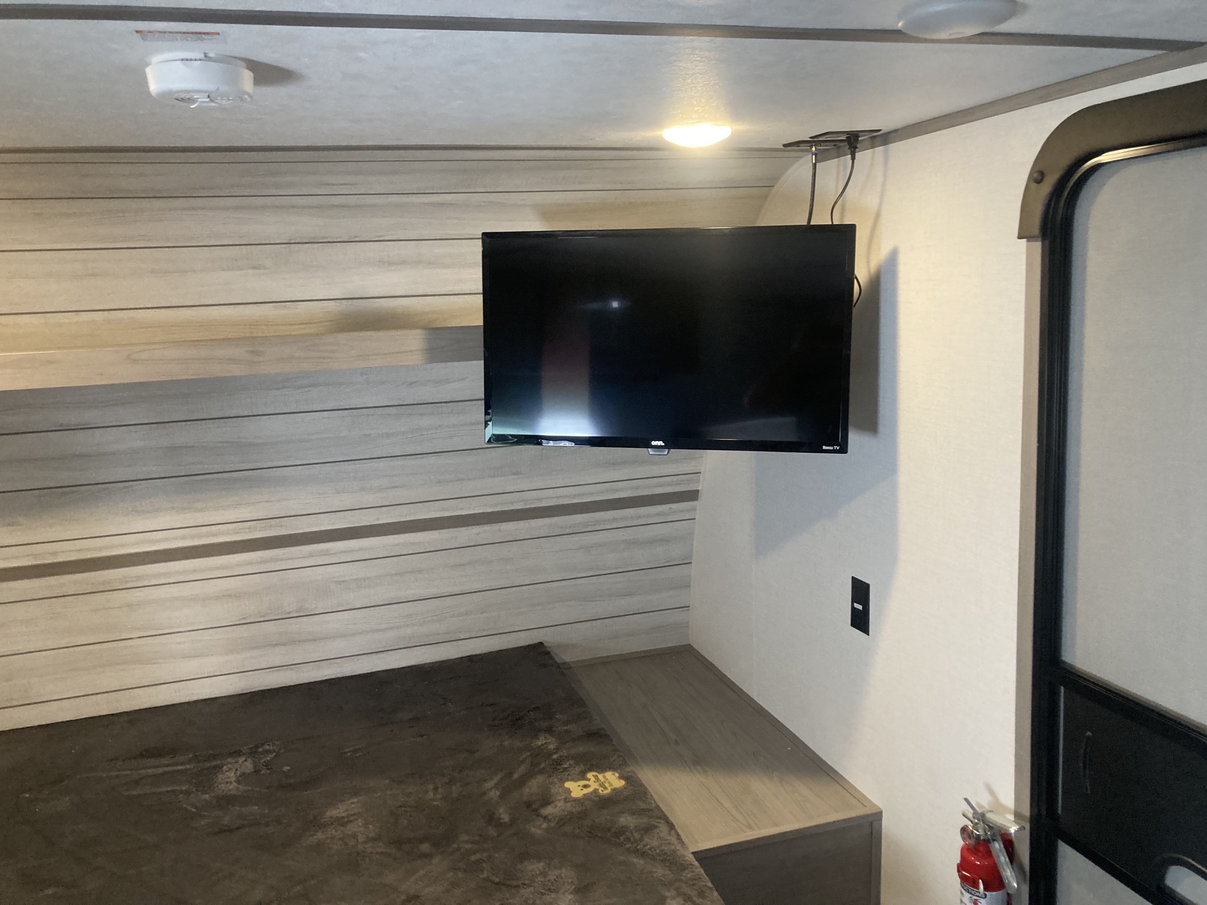 Compact & cozy RV rental interior: a bed, wall-mounted TV, ceiling light, and safety features like a smoke detector & fire extinguisher.. Coleman Lantern 17B 2024