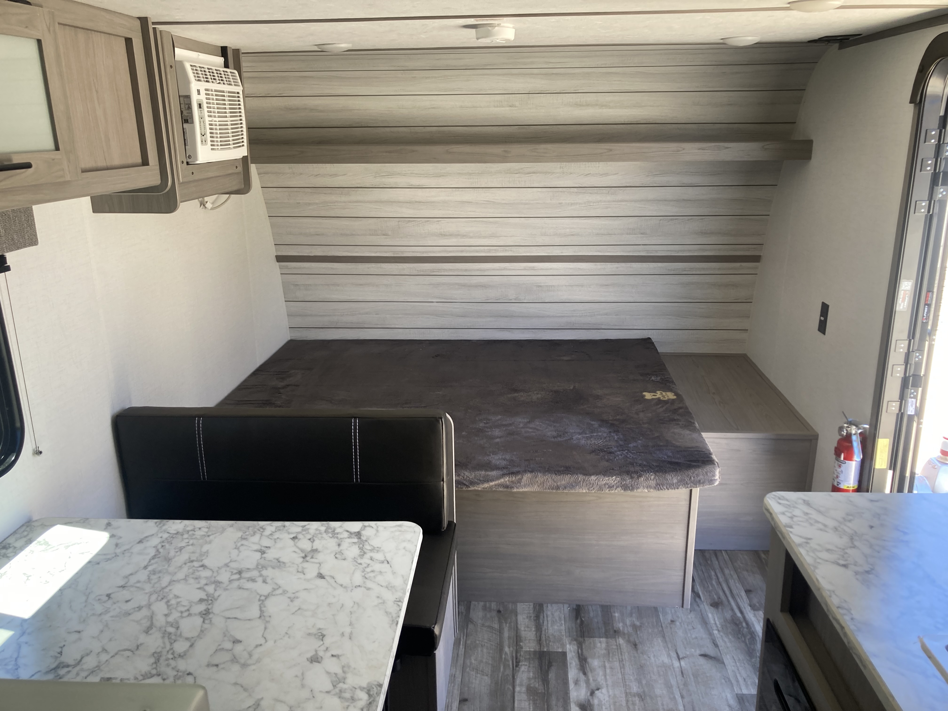 Cozy rv rental interior featuring a grey blanket on the bed, a black dinette with a marble-look table, and an AC unit.. Coleman Lantern 17B 2024