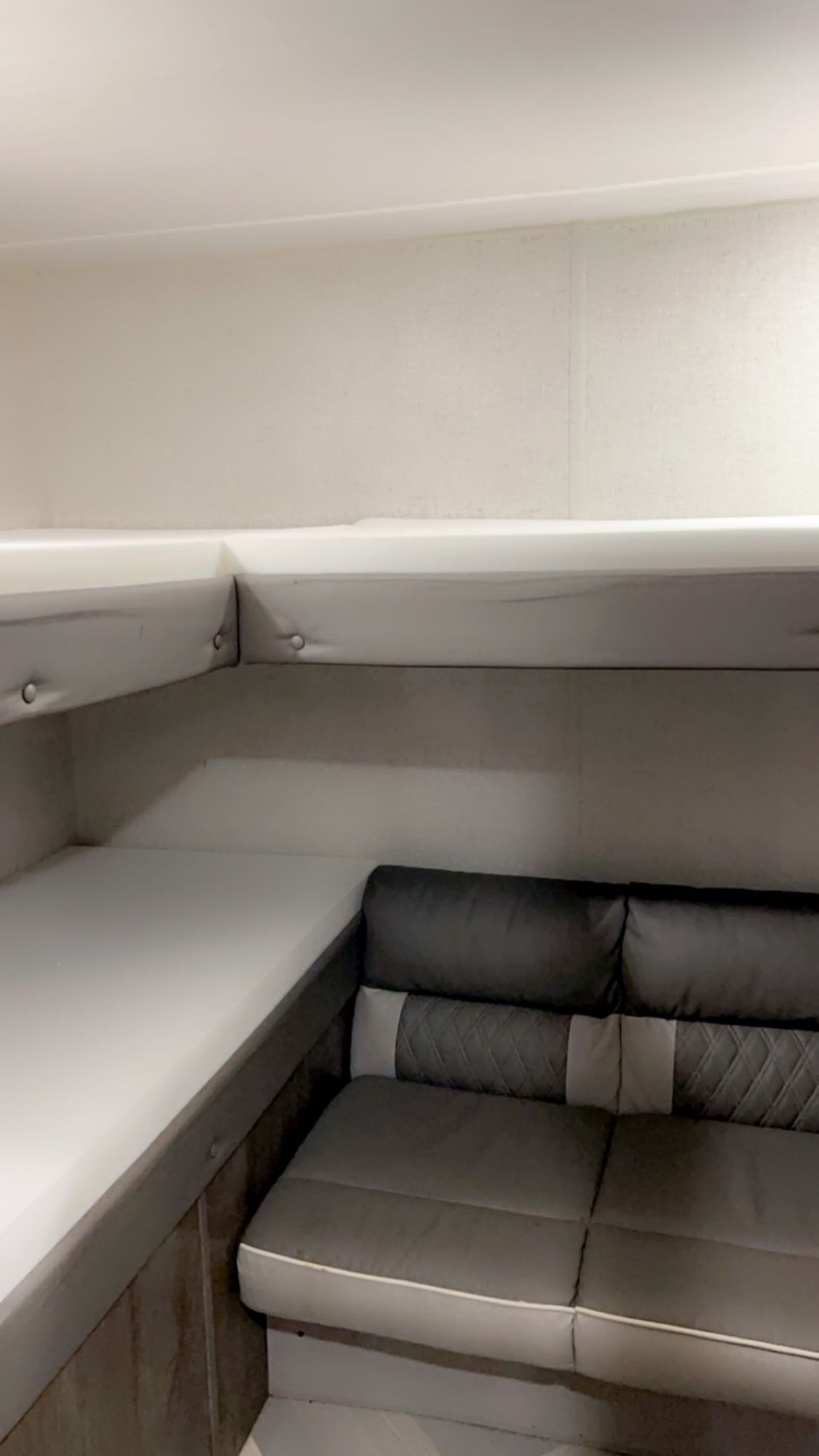 RV rental interior showcasing a modern grey sofa with white trim, set beneath an integrated white bunk or shelf.. Forest River Wildwood X-Lite 2021