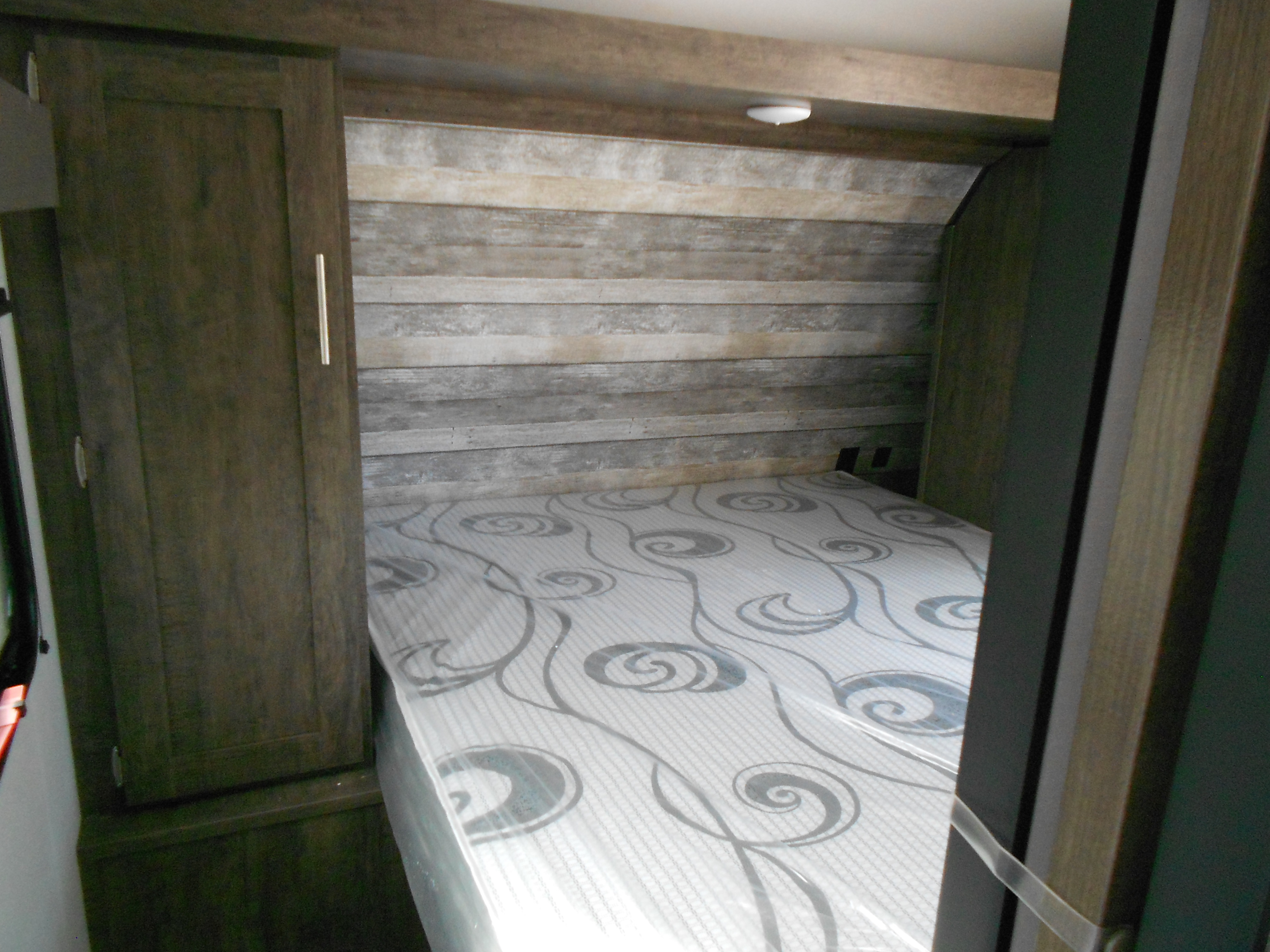 Compact RV rental bedroom with patterned mattress, rustic wood-paneled headboard, and built-in storage on the left.. Xplorer Xplorer 240BHX 2023