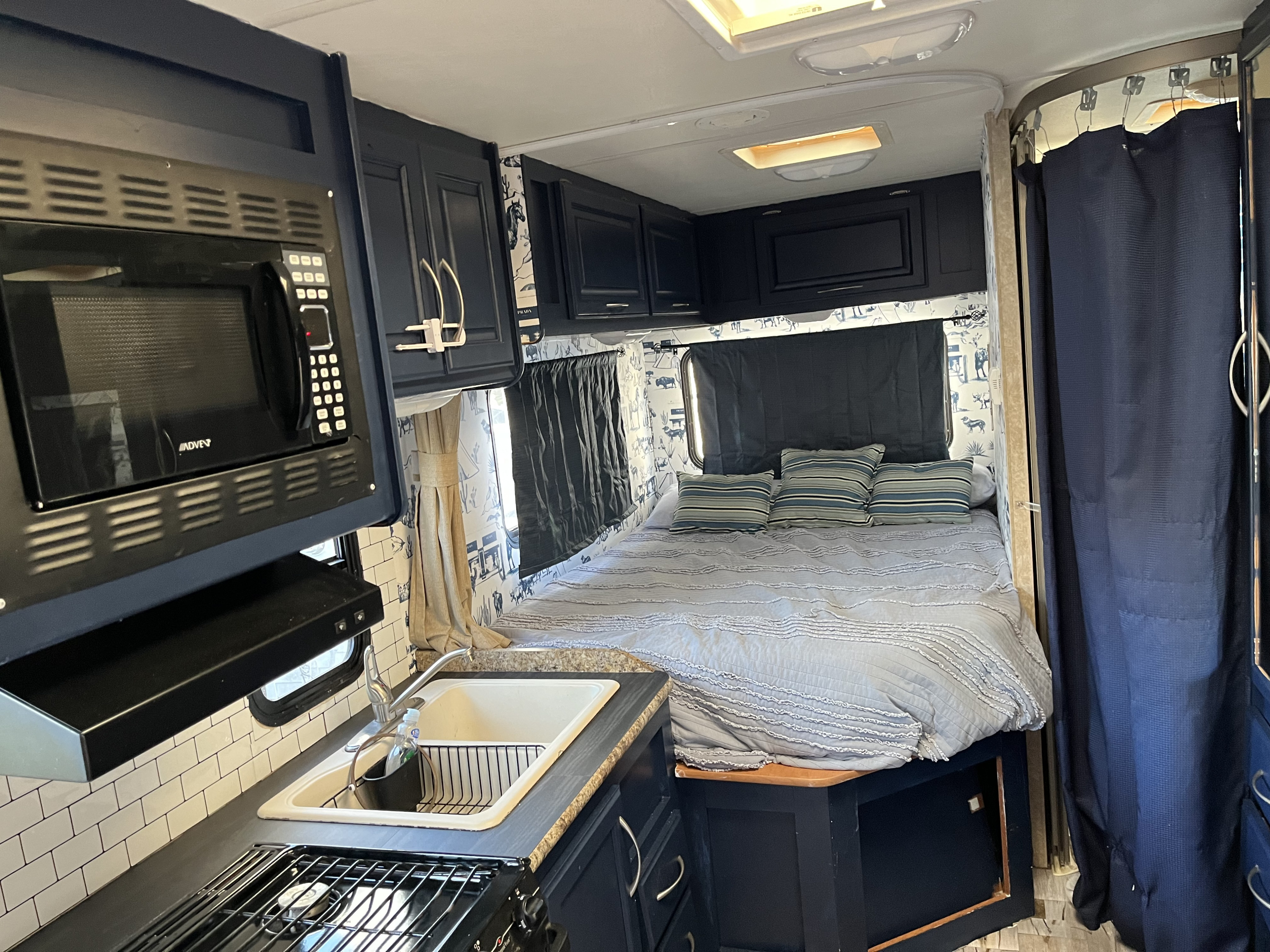 This RV rental interior features a cozy bedroom and compact kitchen with a microwave, sink, and stovetop.. Ford Fourwinds 2011