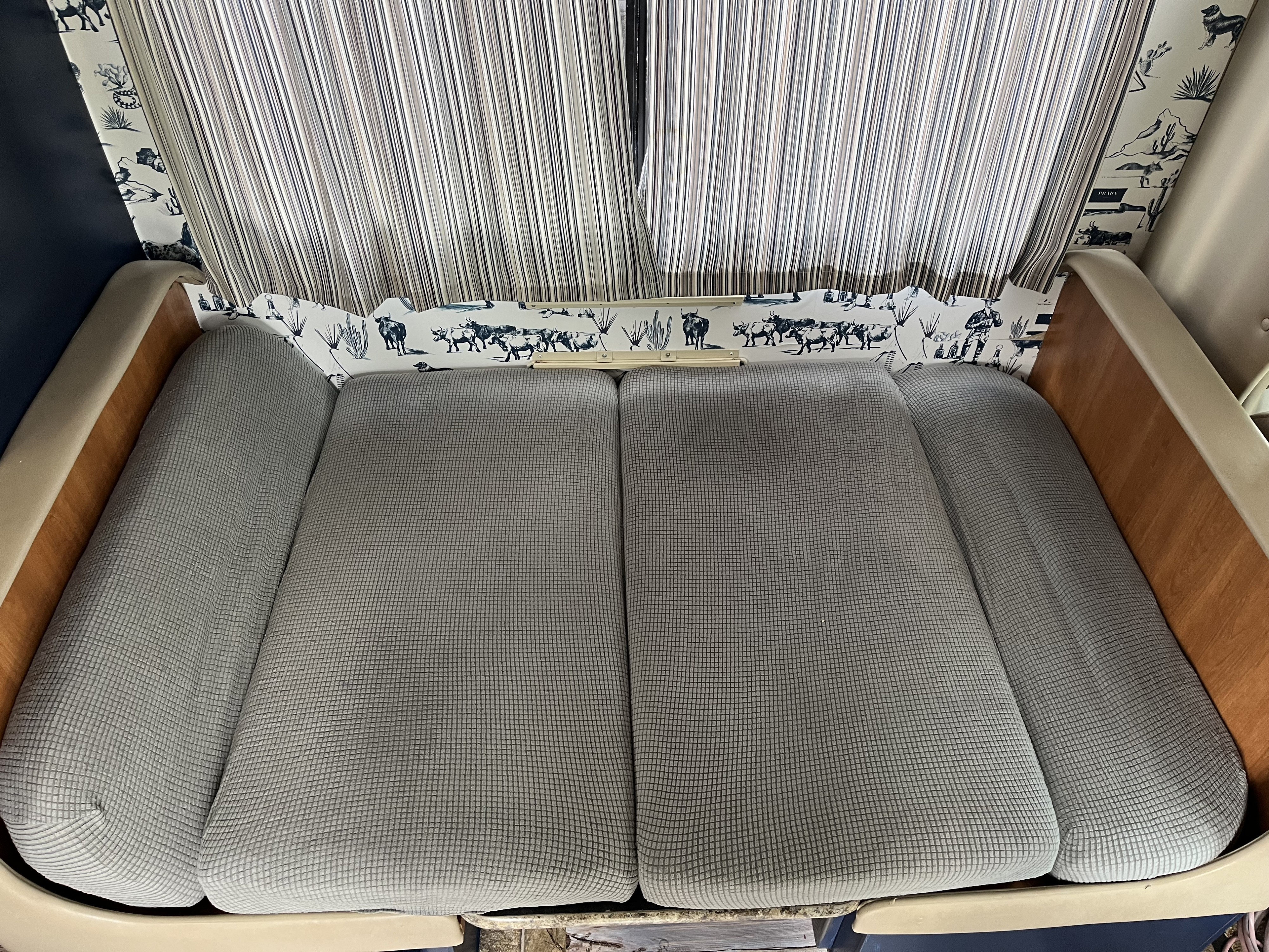 Cozy RV rental interior featuring grey cushions, patterned western-themed wall panels, and striped privacy curtains.. Ford Fourwinds 2011