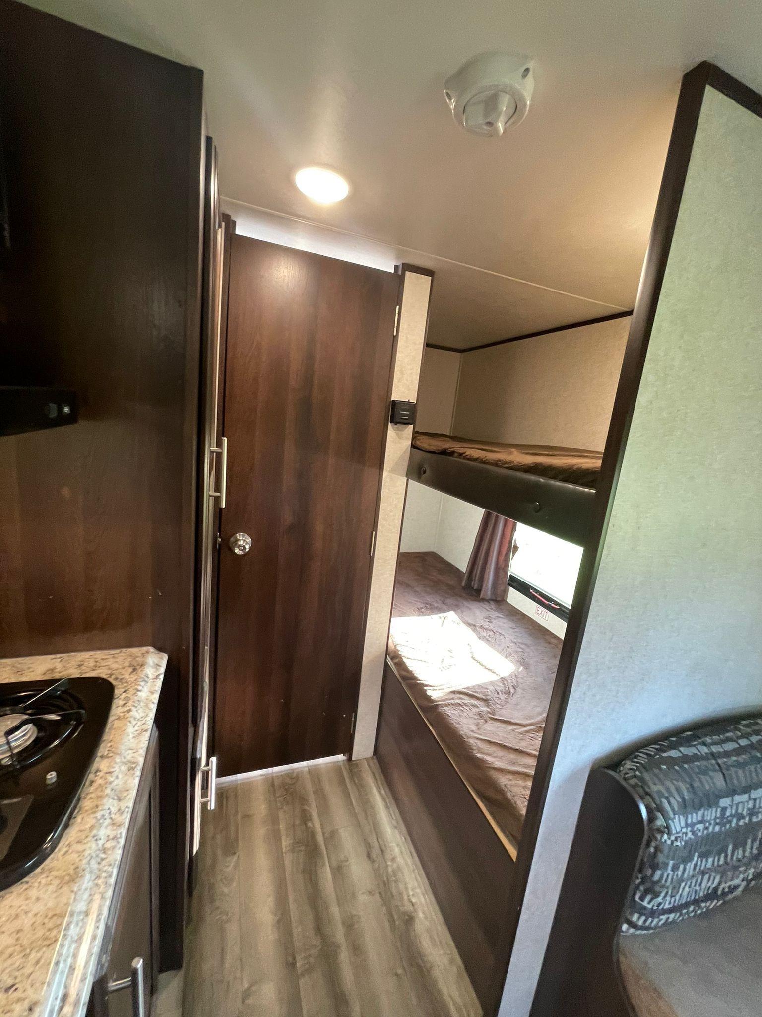 This RV rental interior features a kitchen counter, stove, a closed door, and two built-in bunk beds. A detector is on the ceiling.. Jayco Jay Flight SLX 2019