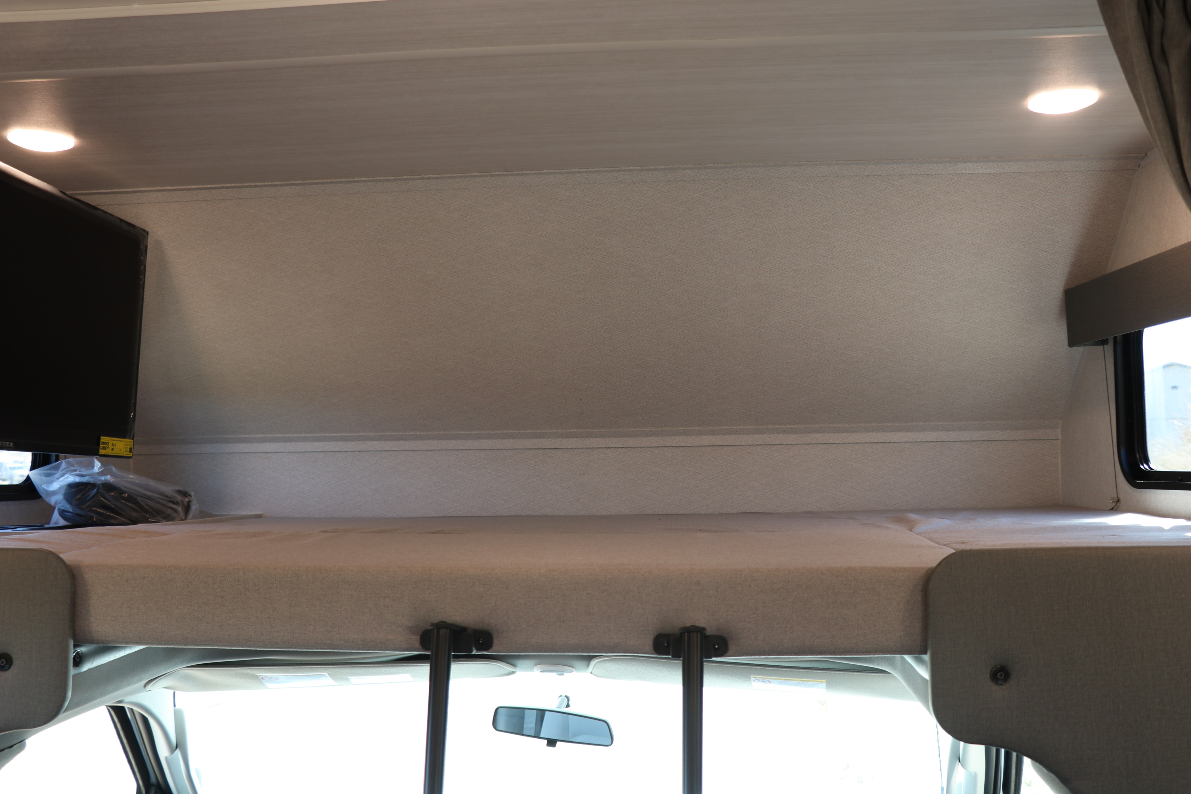 RV rental overhead bunk: A light-colored bed with TV and ceiling lights, overlooking the front cabin. Ideal for travel.. East to West entrada 2025