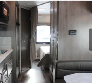 Inside an RV rental: Compact living space with kitchen, private bedroom, and comfortable dining area. Ideal for travel.. Jayco Redhawk 2023