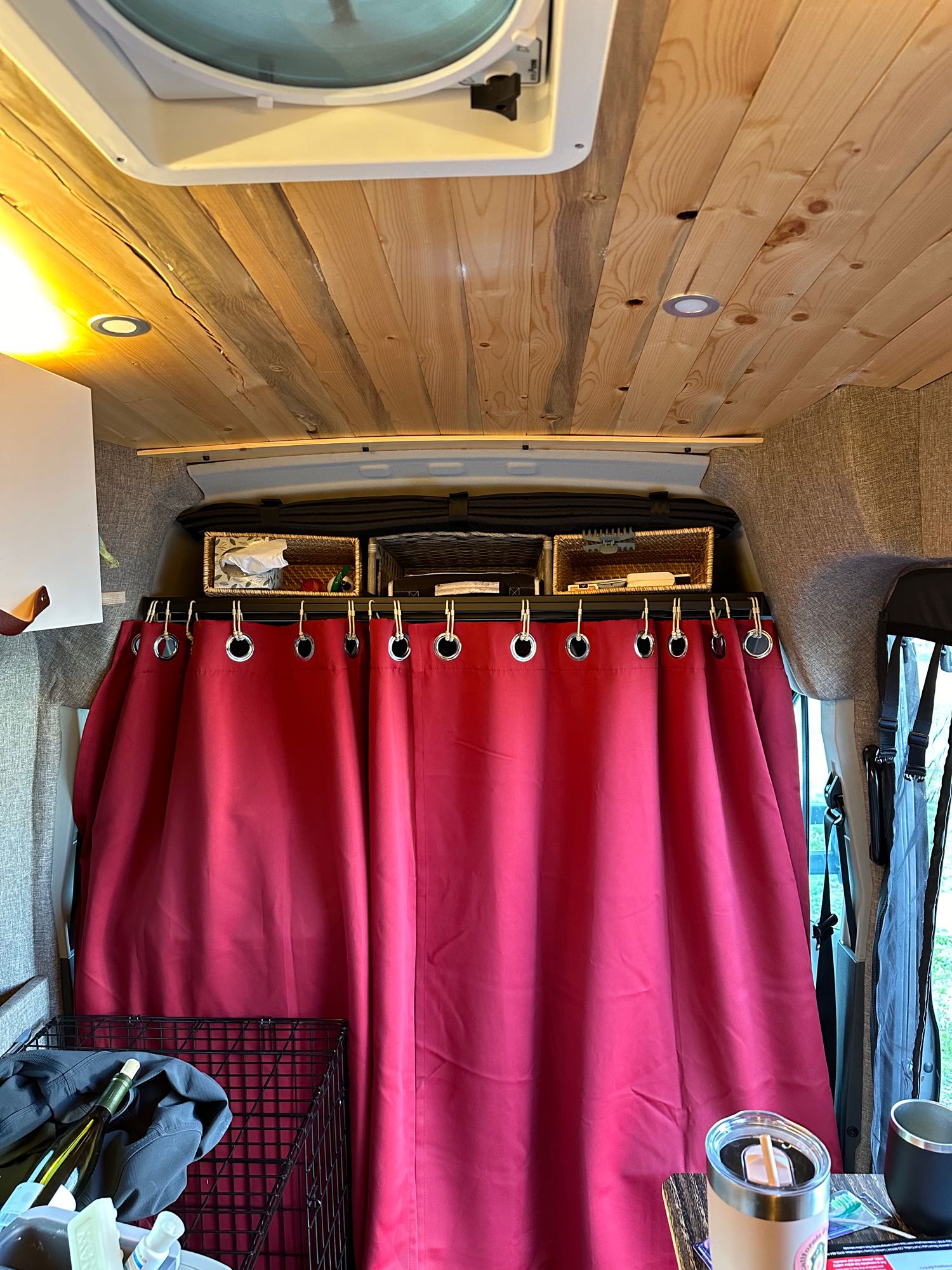 Cozy RV rental interior: wood plank ceiling, overhead storage baskets, and a vibrant red privacy curtain.. Ford Transit 2020