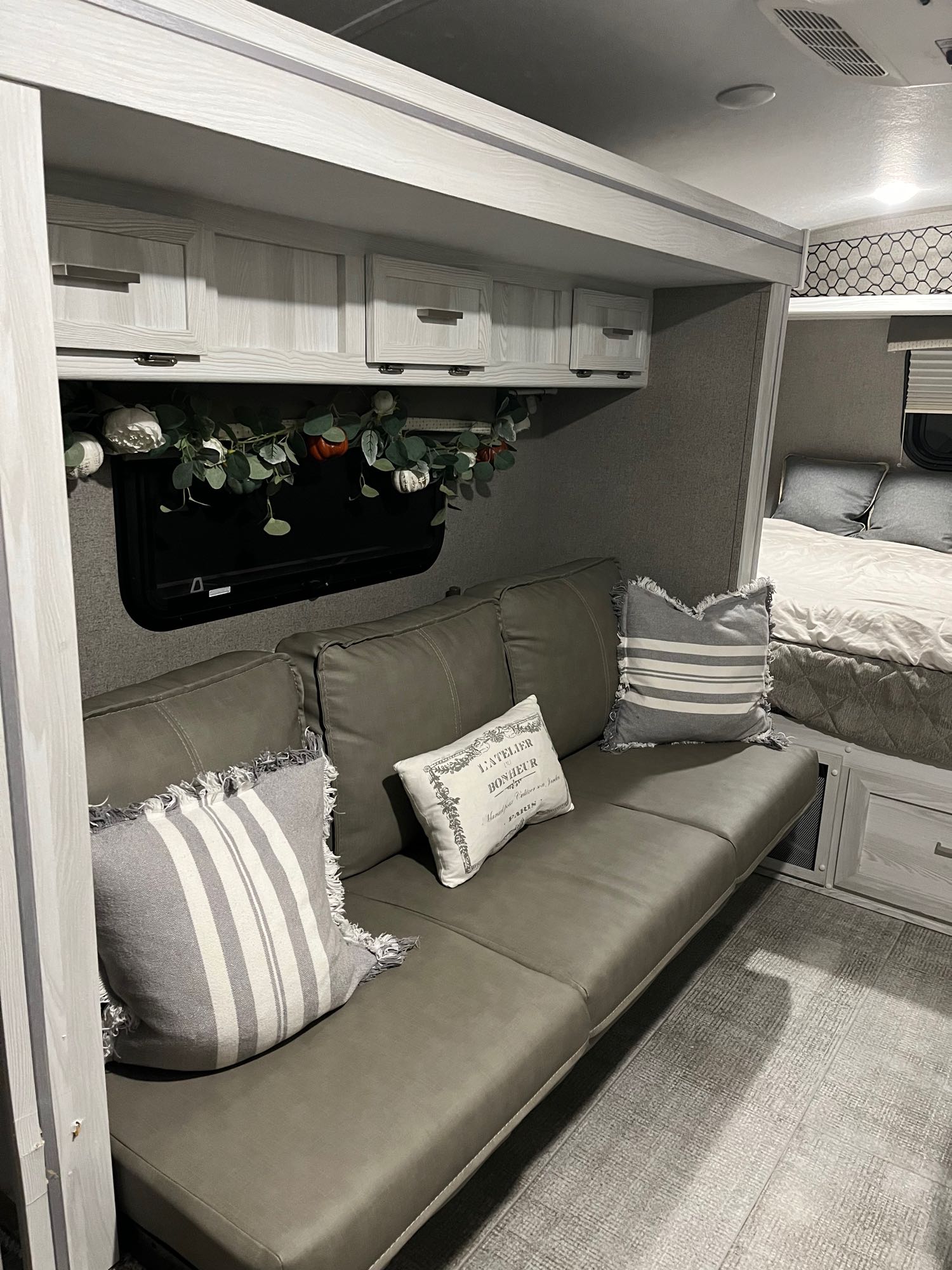 Inside an RV rental: a modern living area with a gray sofa, overhead cabinets, and a peek into the bedroom.. Forest River Rockwood Geo Pro 2021