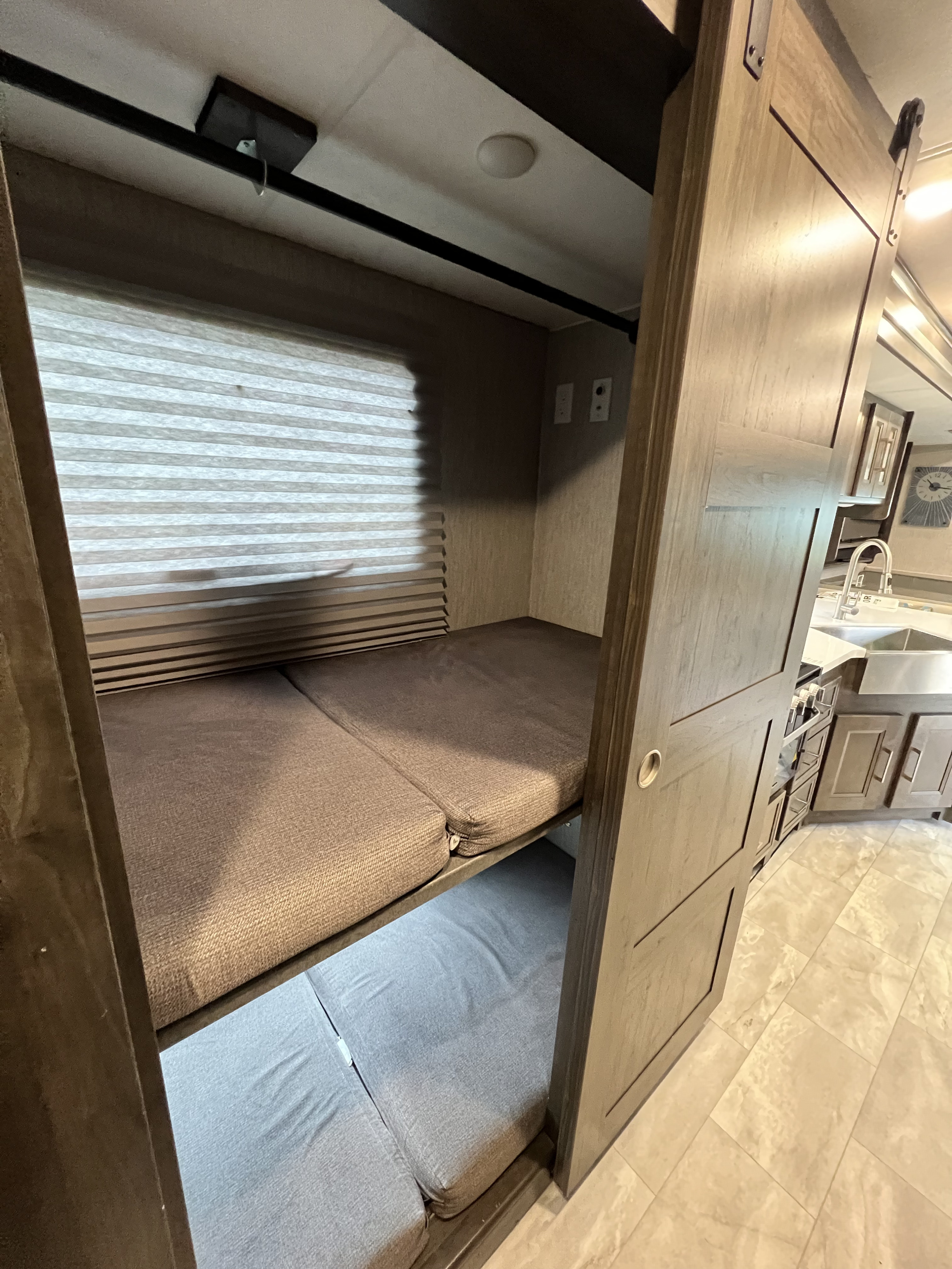RV rental interior featuring cozy bunk beds, a window with blinds, and a peek into the compact kitchen area.. Forest River Coachmen Sportscoach SRS 2021