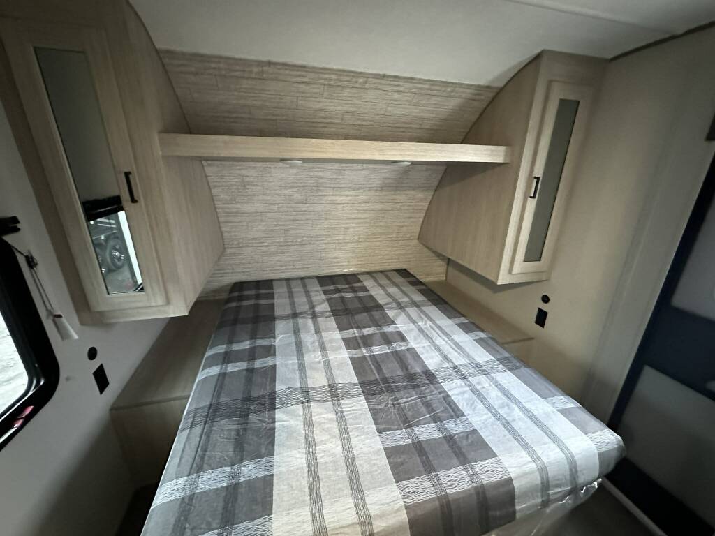 Cozy RV rental bedroom featuring a plaid bed, overhead storage, and textured wall for comfortable travel.. Forest River Catalina 2024