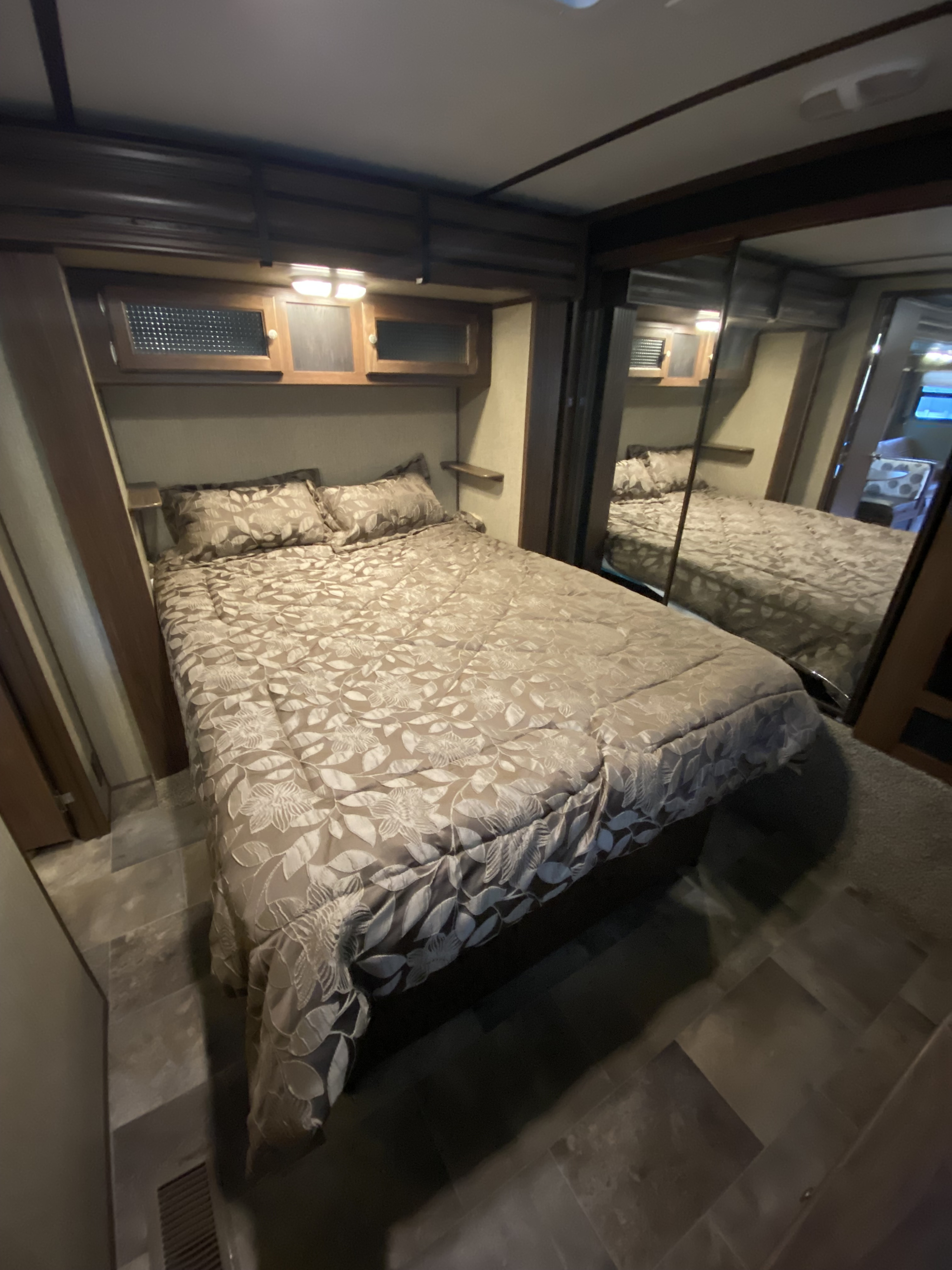 Cozy RV rental bedroom featuring patterned bedding, overhead storage, and mirrored wardrobe for a comfortable journey.. Keystone RV Sprinter Campfire Edition 2018