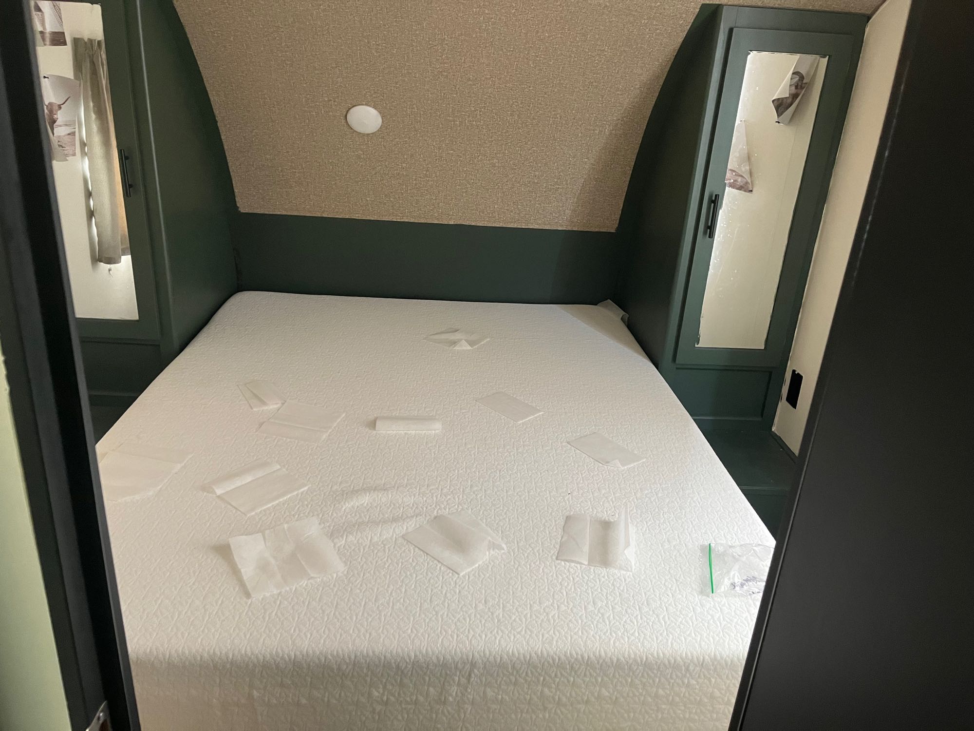 An RV rental bedroom with a white mattress, dark green cabinets with mirrors, and a textured ceiling. Small white squares on the bed.. Forest River Cherokee Grey Wolf 2017