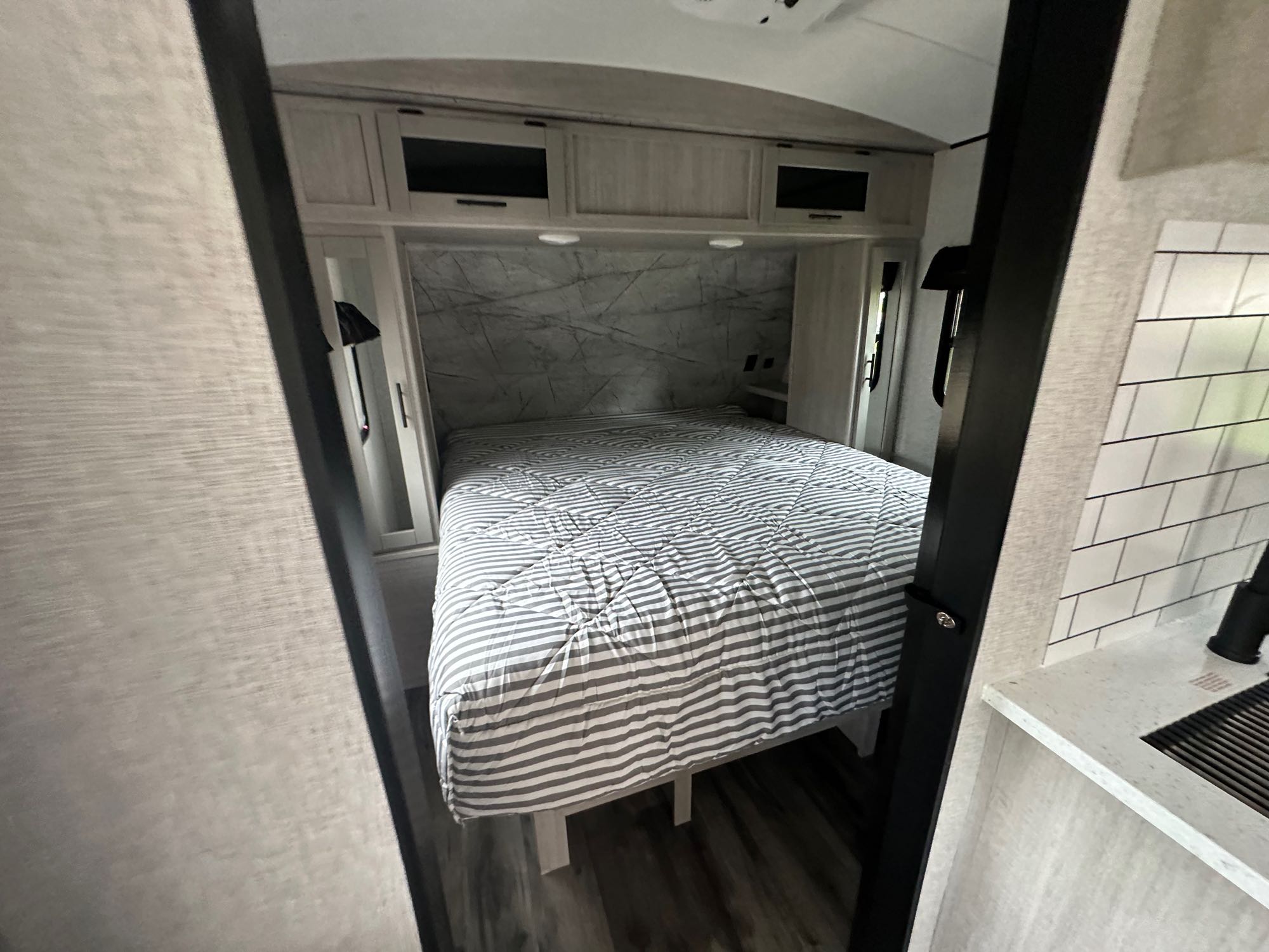 Inside an RV rental: a compact bedroom with a striped bed, light wood cabinets, and marbled headboard wall. Perfect for road trips.. Crossroads RV Sunset Trail Superlite 2024