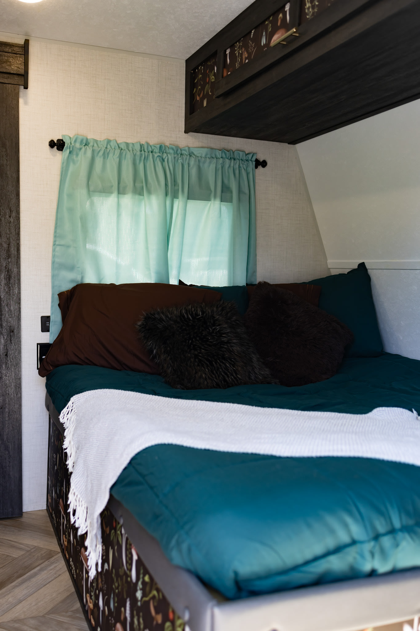 Cozy RV bedroom features teal bedding, plush pillows, and custom mushroom decor, ideal for your next RV rental.. Forest River Ozark 2022