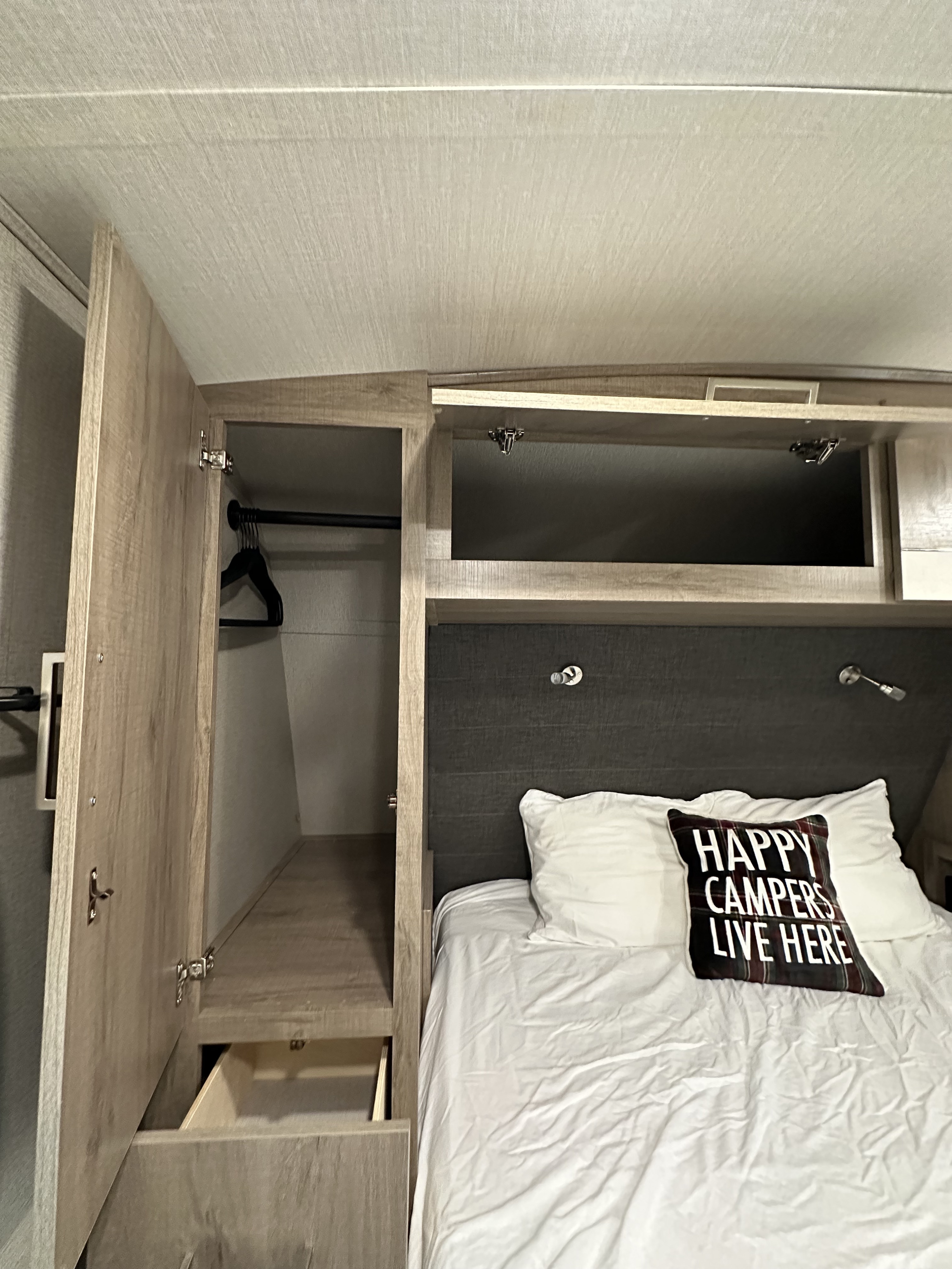RV rental bedroom featuring a bed with a 'Happy Campers' pillow, open closet, and overhead storage.. Grand Design Imagine 2022