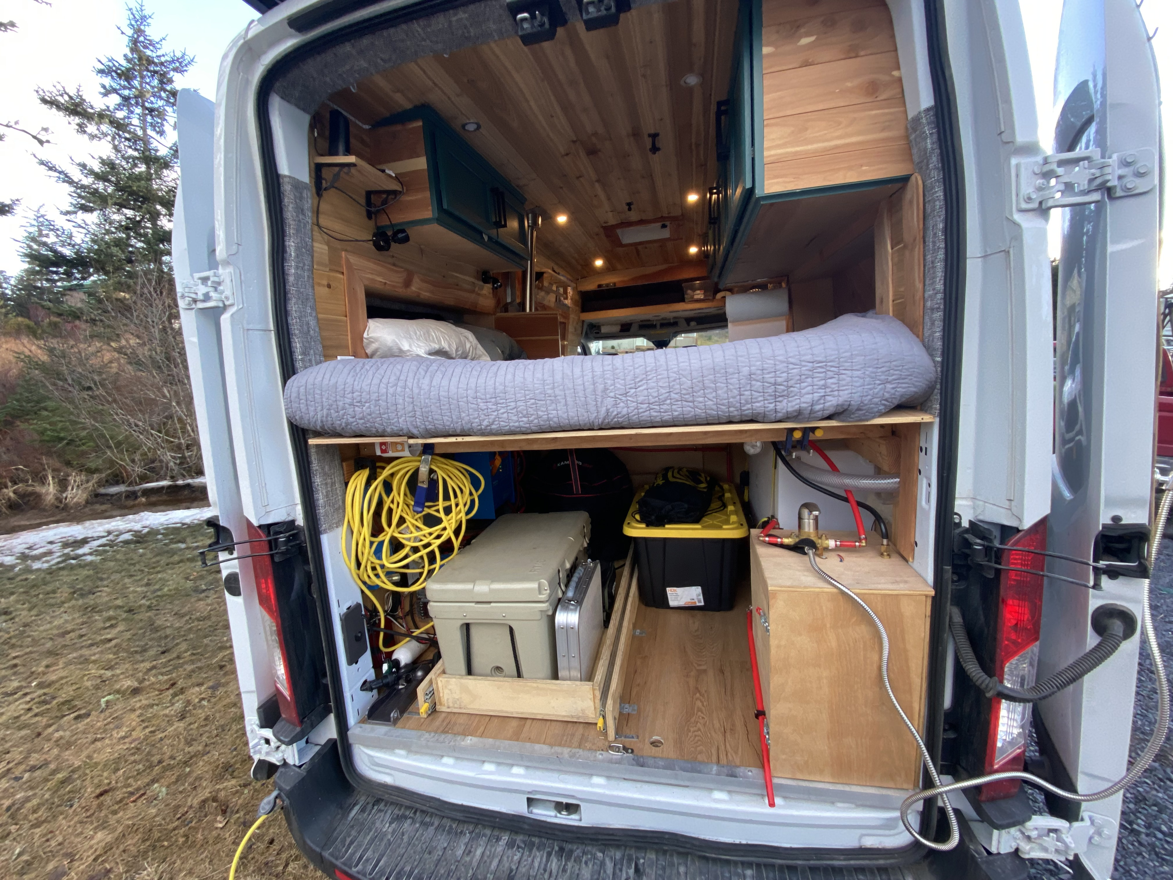 RV rental camper van's open rear reveals a custom interior with bed, storage, and water system for adventure.. Ford Transit 2020
