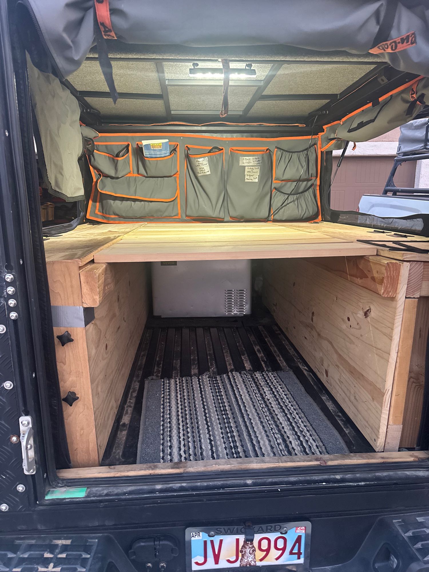 Interior view of a DIY truck bed camper build, ideal for RV rental. Features a custom wooden platform, portable fridge, and storage organizers.. Toyota Tacoma 2022