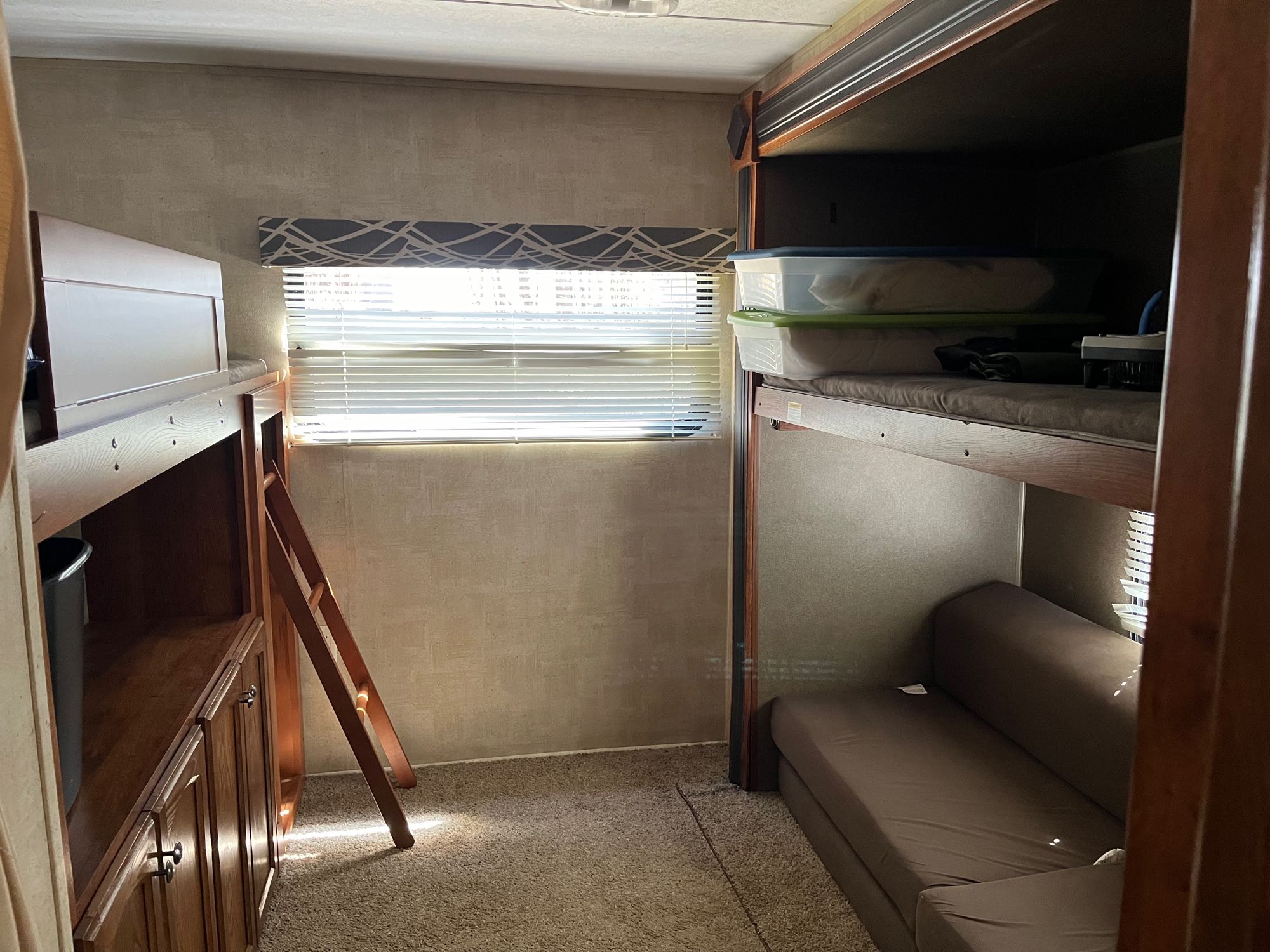 Inside a cozy RV rental bunkhouse with two bunk beds, a ladder, window, and wood storage cabinets.. Keystone RV Hideout 2015