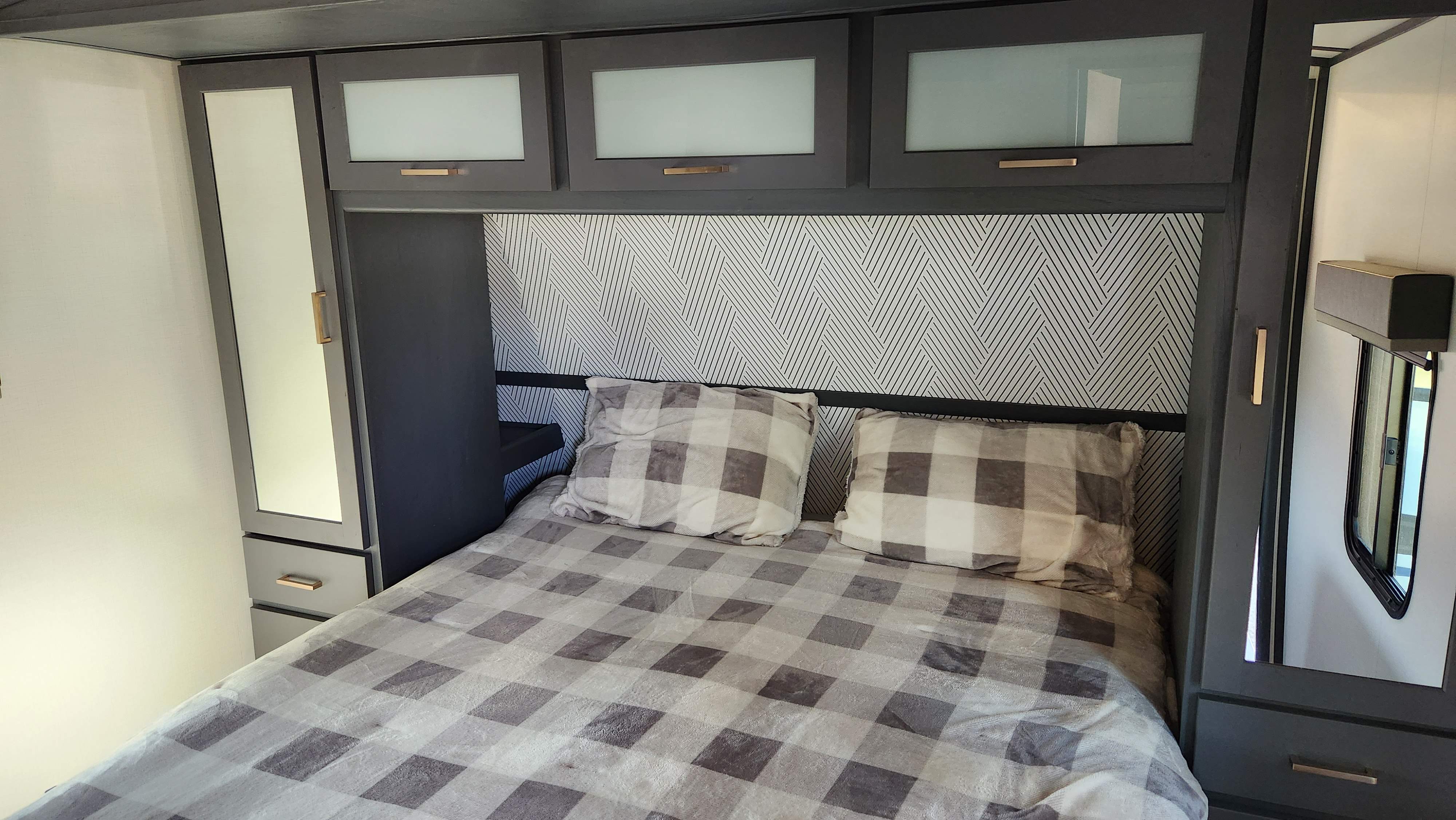 Interior view of a modern RV rental bedroom featuring a plaid bed, geometric headboard, and sleek storage cabinetry.. Keystone RV Bullet Premier Ultra Lite 2022