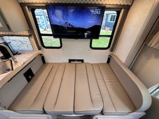 Explore this RV rental's versatile interior: a beige cushioned convertible bed/dinette with mounted TV and windows, ideal for travel.. Thor Coleman 2024
