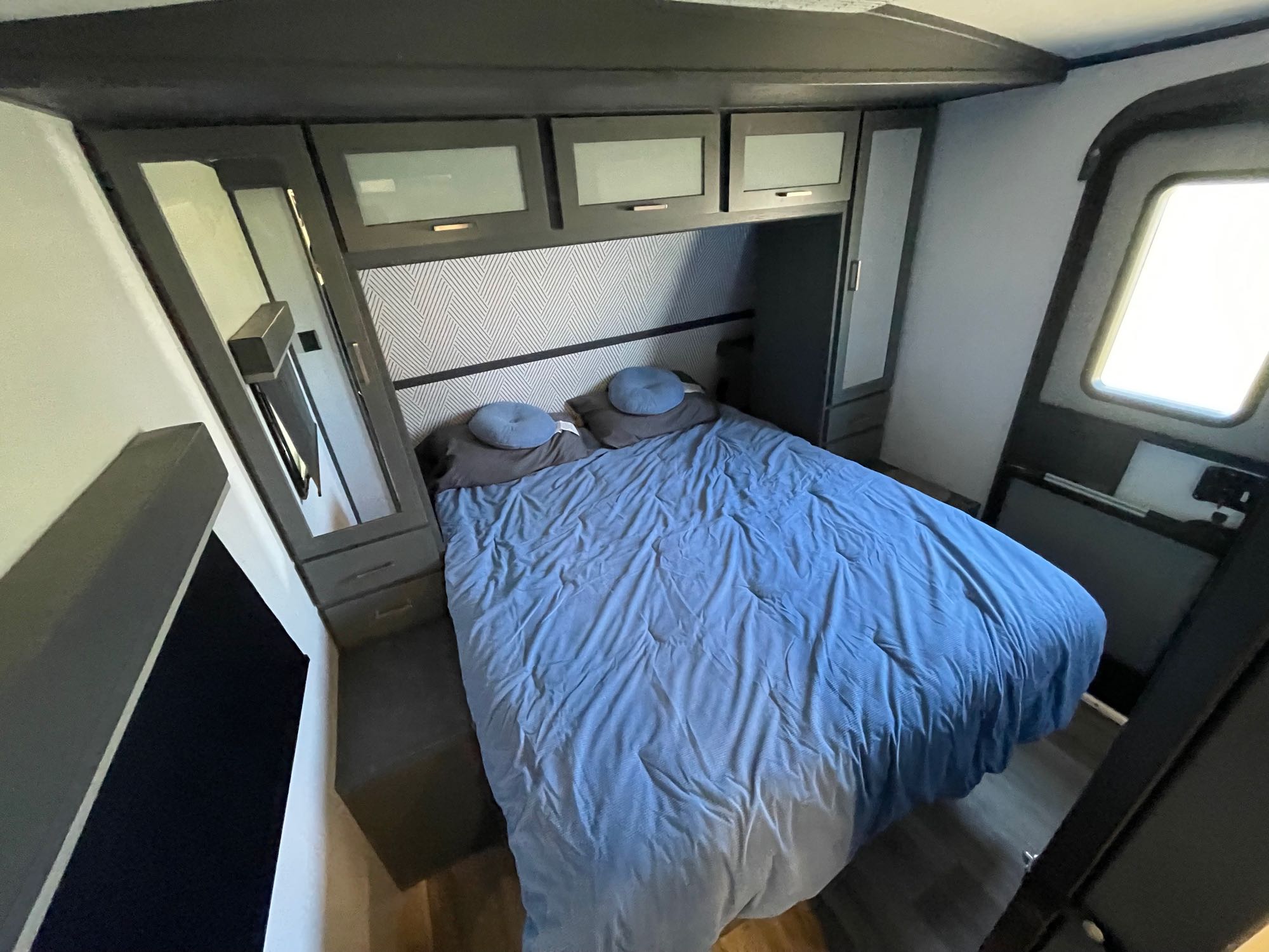 An RV rental bedroom features a blue bed, ample dark wood storage, and a mirrored wardrobe for comfortable stays.. Keystone RV Bullet Premier Ultra Lite 2022