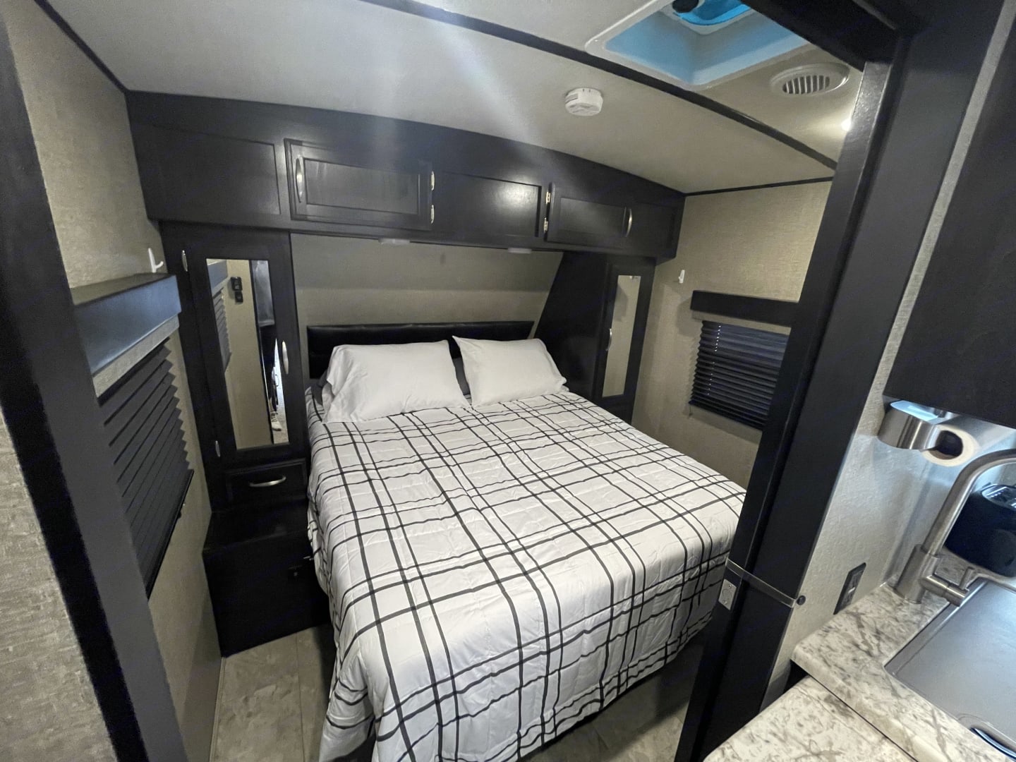 RV rental bedroom interior: a modern, compact space with a neatly made bed, overhead storage, and windows.. Grand Design Imagine 2019