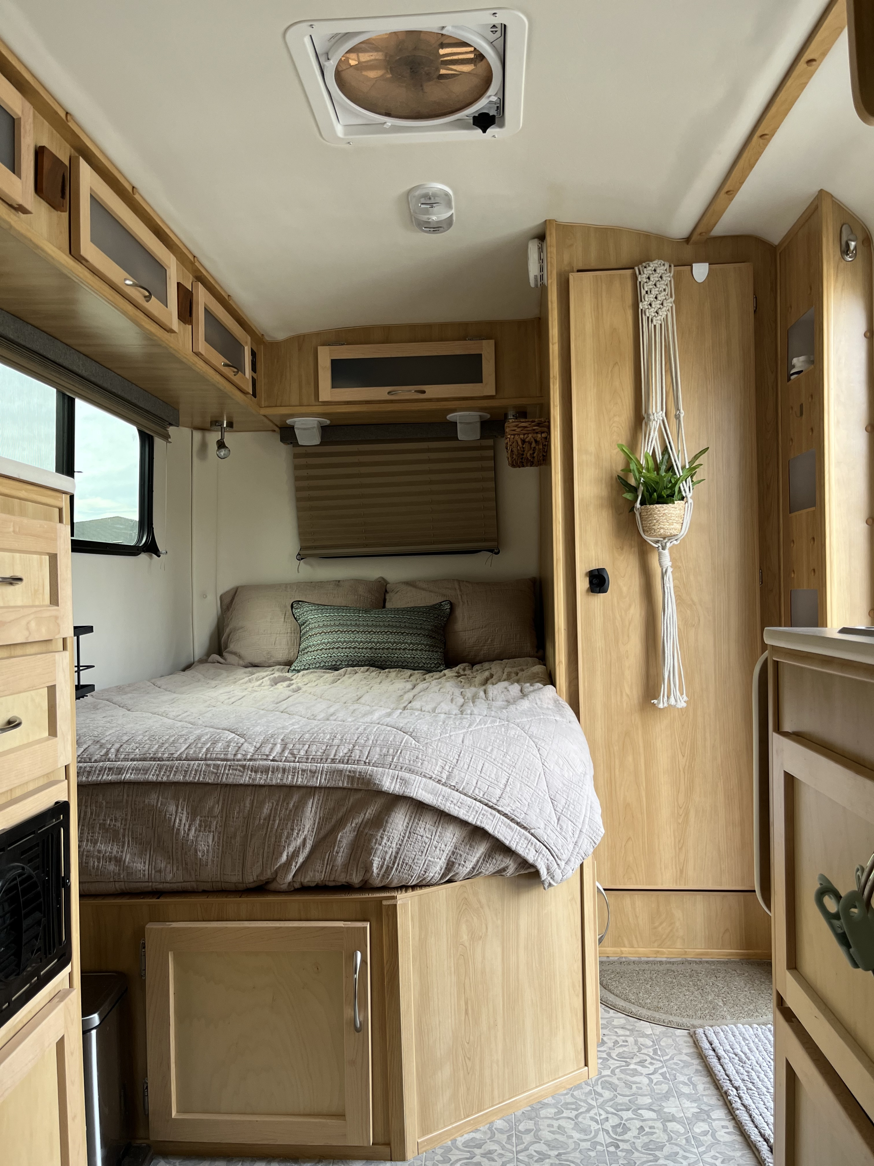 Cozy RV rental bedroom featuring a comfortable bed, light wood cabinetry, ceiling fan, and a plant for compact living.. Escape Trailer Escape Trailer Trailer 2022