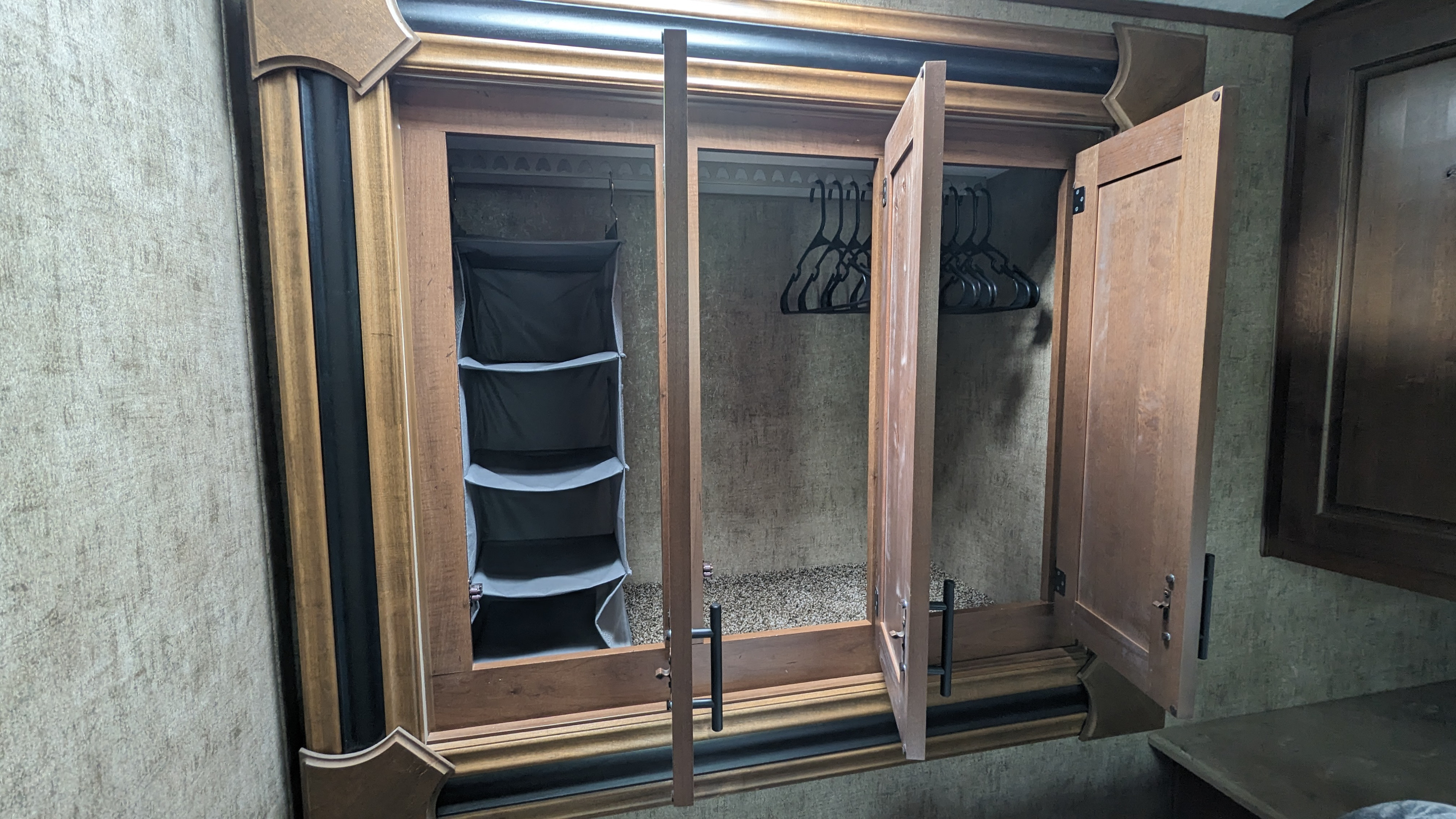 Open RV closet with a multi-tiered hanging organizer on the left and black hangers on rods, perfect for an RV rental.. Outdoors RV Blackstone Titanium 2023