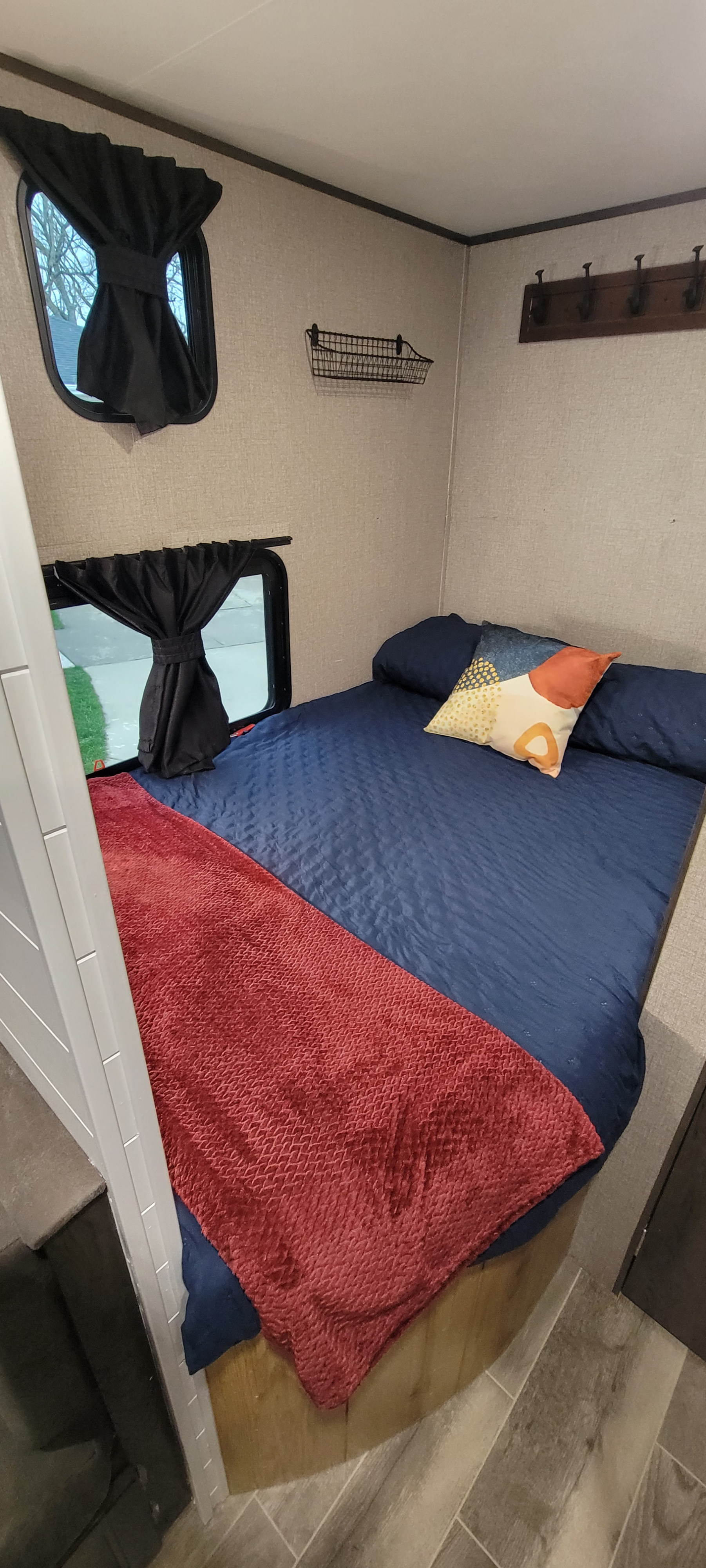 Cozy RV rental bedroom features a blue bed, red throw, compact windows, wall storage, and coat rack.. Jayco Jay Flight SLX 2021