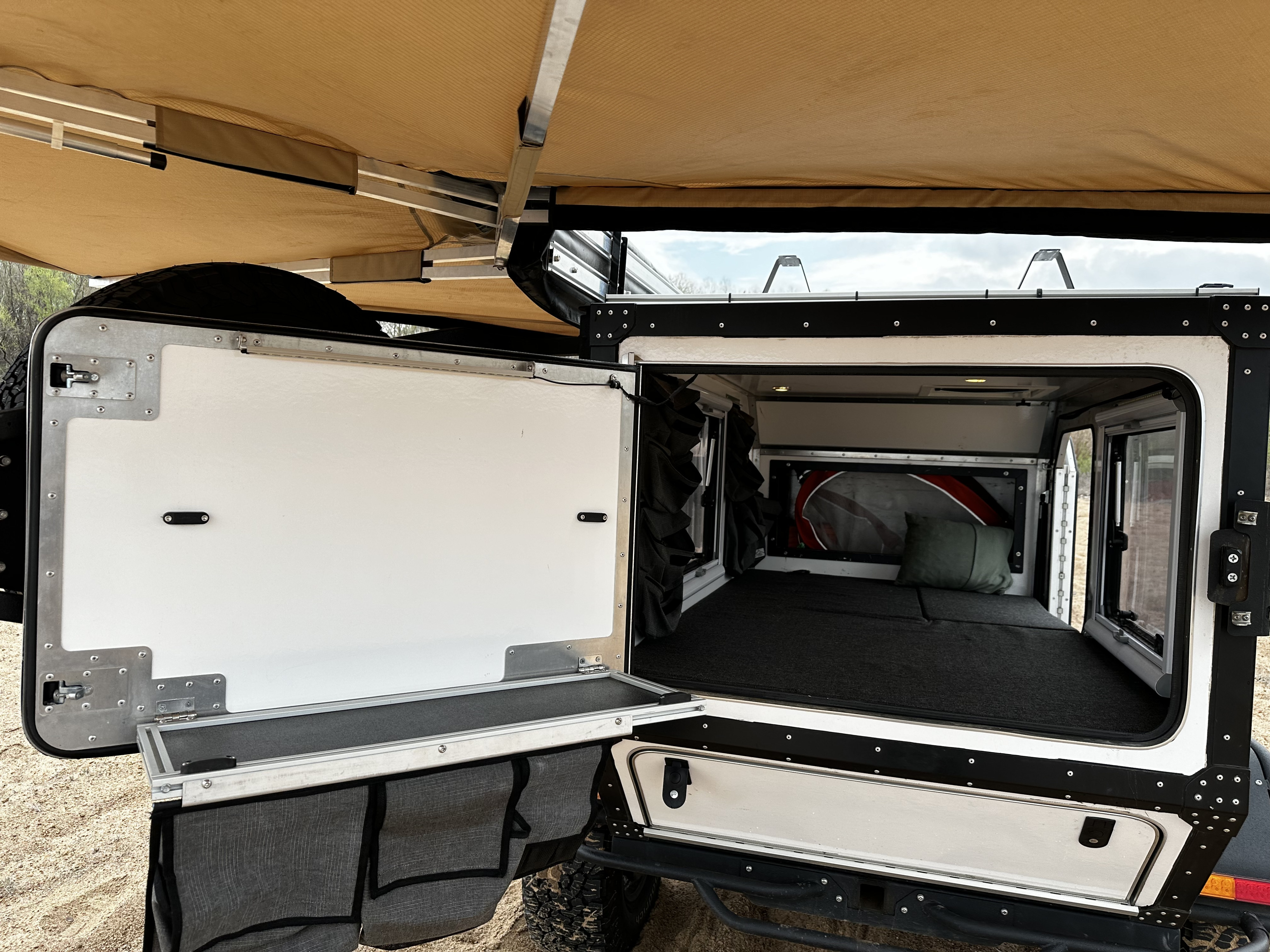 An open off-road camper interior, showing the bed, storage, and an extended awning. Ideal for your next rv rental adventure.. Overkill Tk47 2020