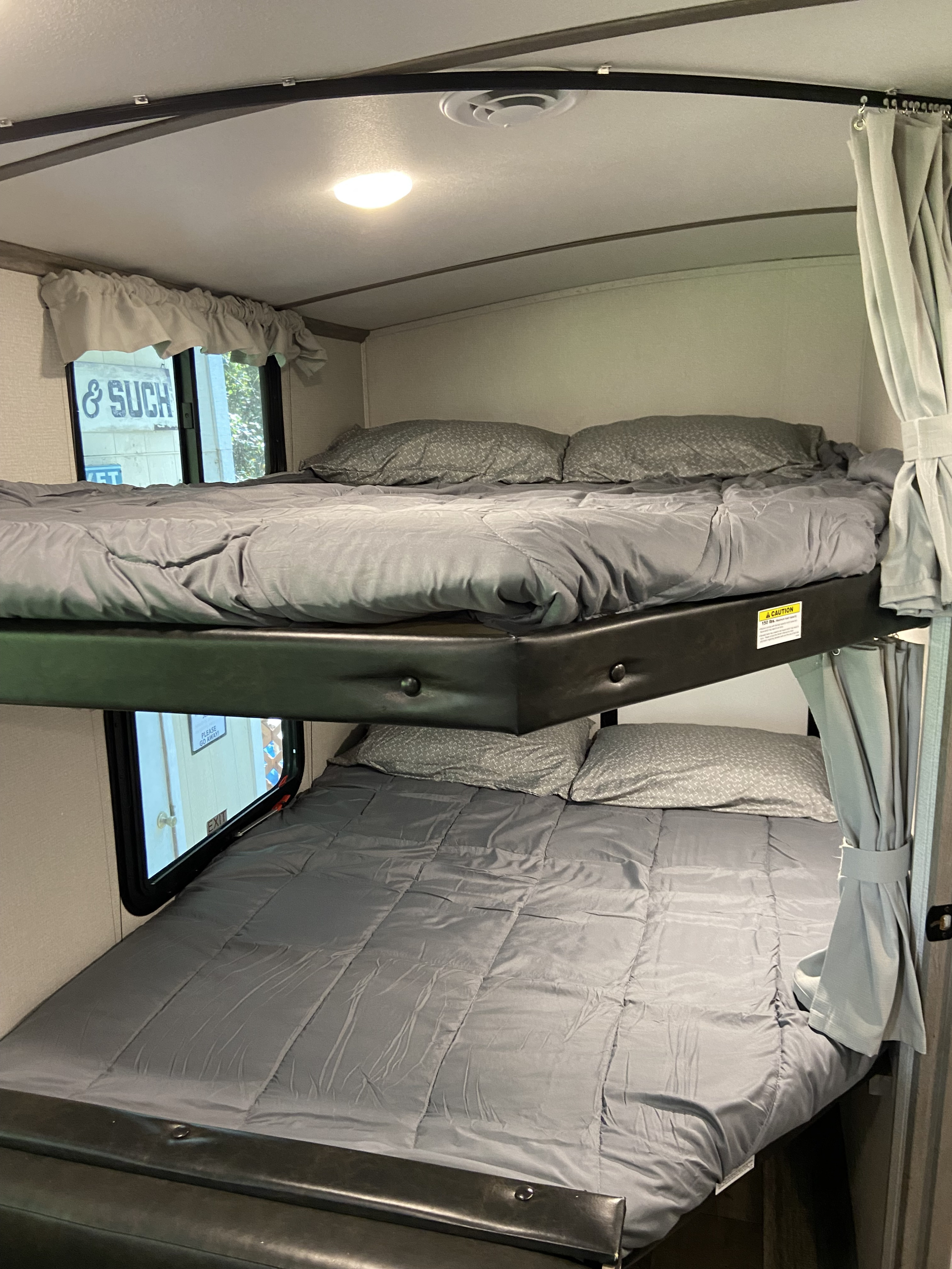 This RV rental features comfortable bunk beds with grey bedding and privacy curtains, ideal for family travel.. Keystone RV Outback 2021