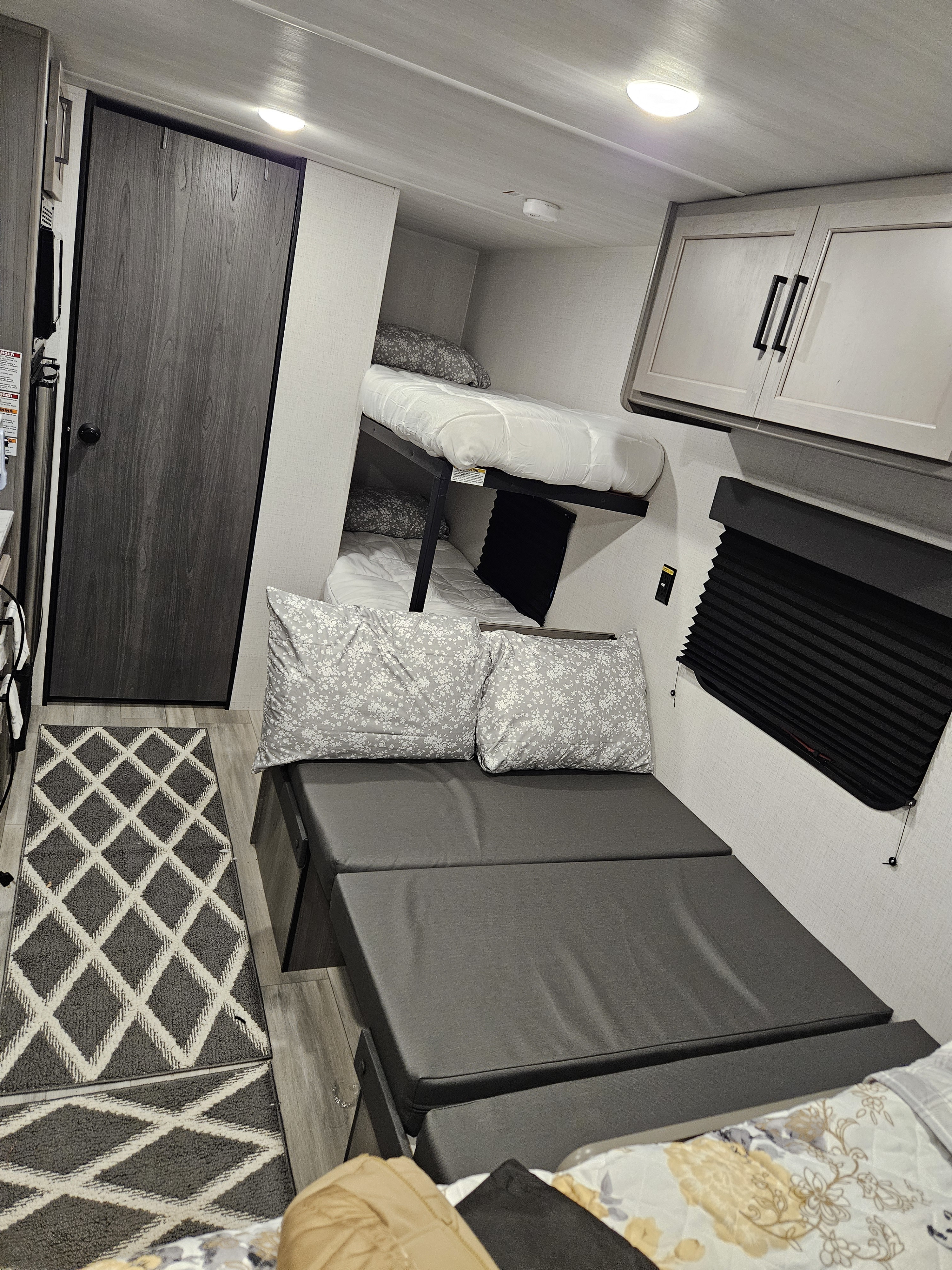 This RV rental interior features practical bunk beds, a gray convertible sofa, and overhead storage, designed for comfortable travel.. Keystone RV Keystone Hideout 175BH 2024