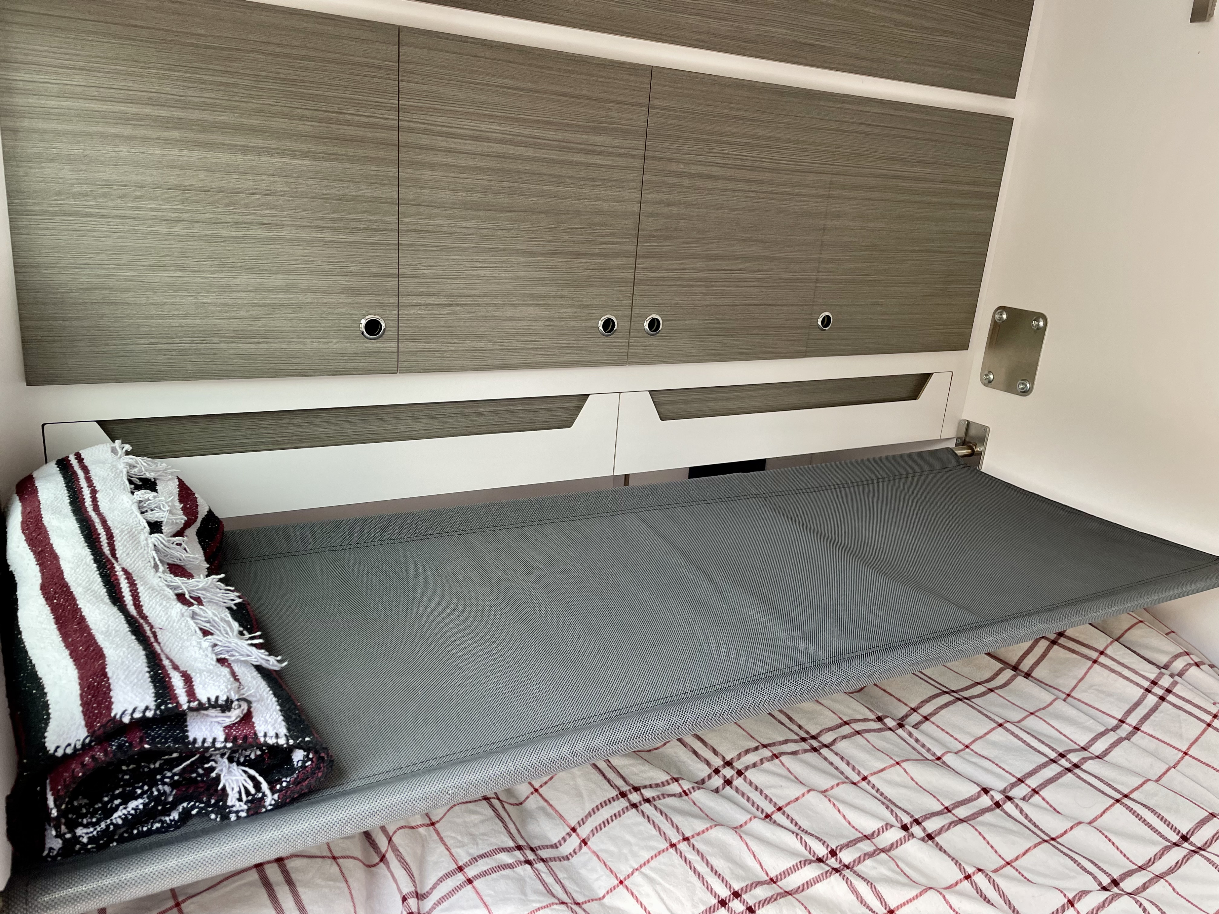Compact RV rental interior with a grey mesh bunk bed, wood-grain cabinets, and plaid bedding, designed for efficient travel.. Bean Bean Stock 2021