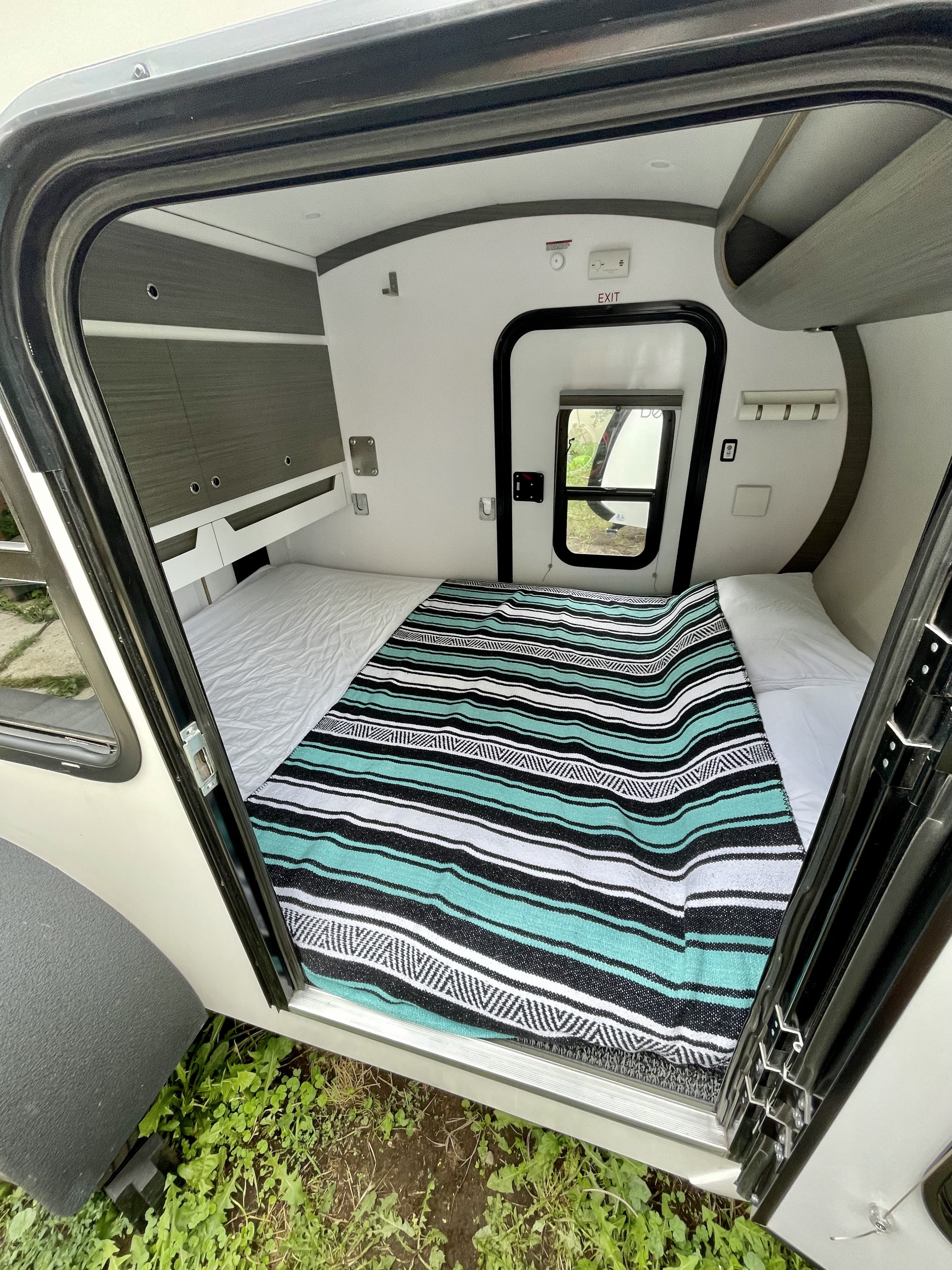 View into a modern RV rental sleeping area with a striped blanket, white sheets, and built-in storage cabinets.. Bean Bean Stock 2021