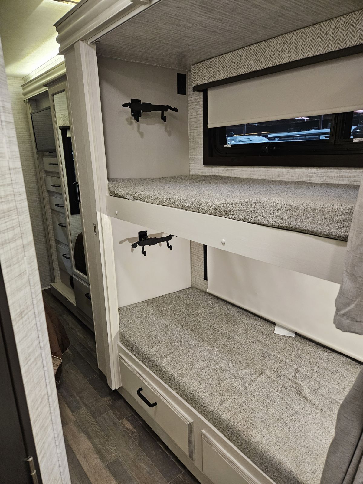 Compact RV rental bunk beds with soft mattresses, a window, and a nearby storage cabinet, perfect for families.. Thor Vision 2024