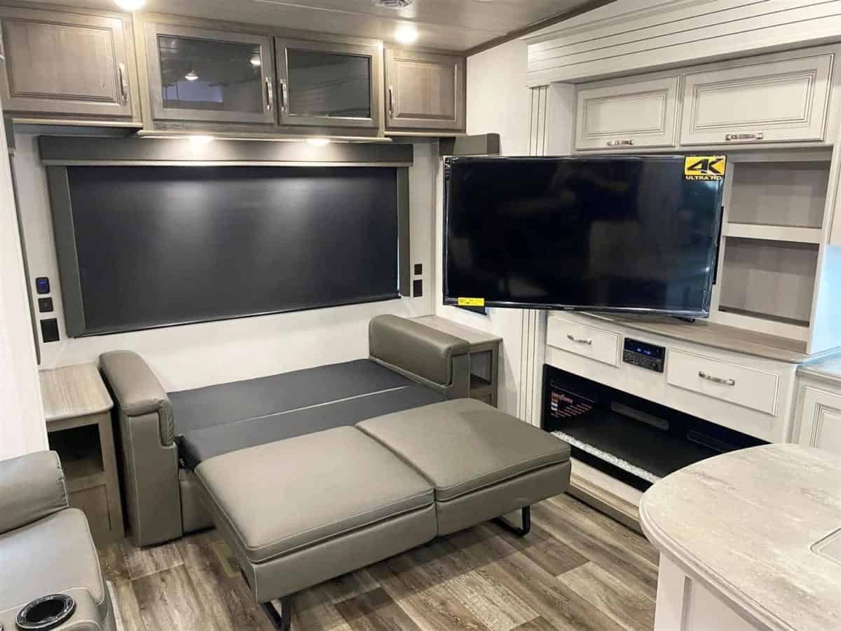 Modern RV rental living area with convertible sofa bed, large window shade, TV, and fireplace below cabinets.. Keystone Cougar 2022