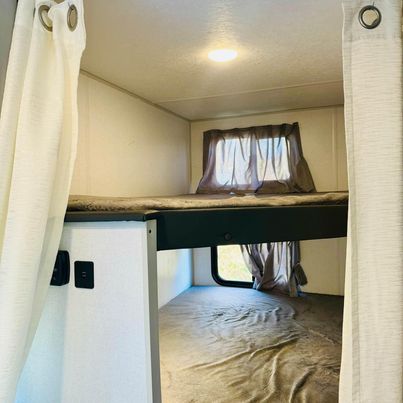 RV rental bunk beds feature privacy curtains, windows, and outlets, offering a comfortable sleeping area for travelers.. Forest River Wildwood FSX 2021