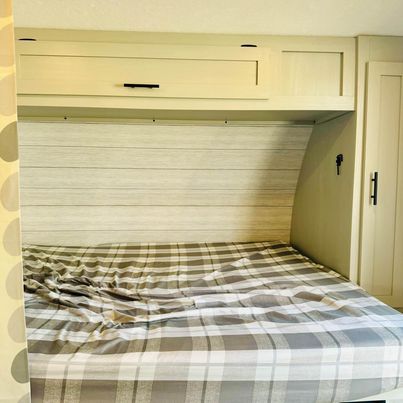 RV rental bedroom: a cozy space with a plaid bed, light wood overhead cabinets, and shiplap accent wall.. Forest River Wildwood FSX 2021