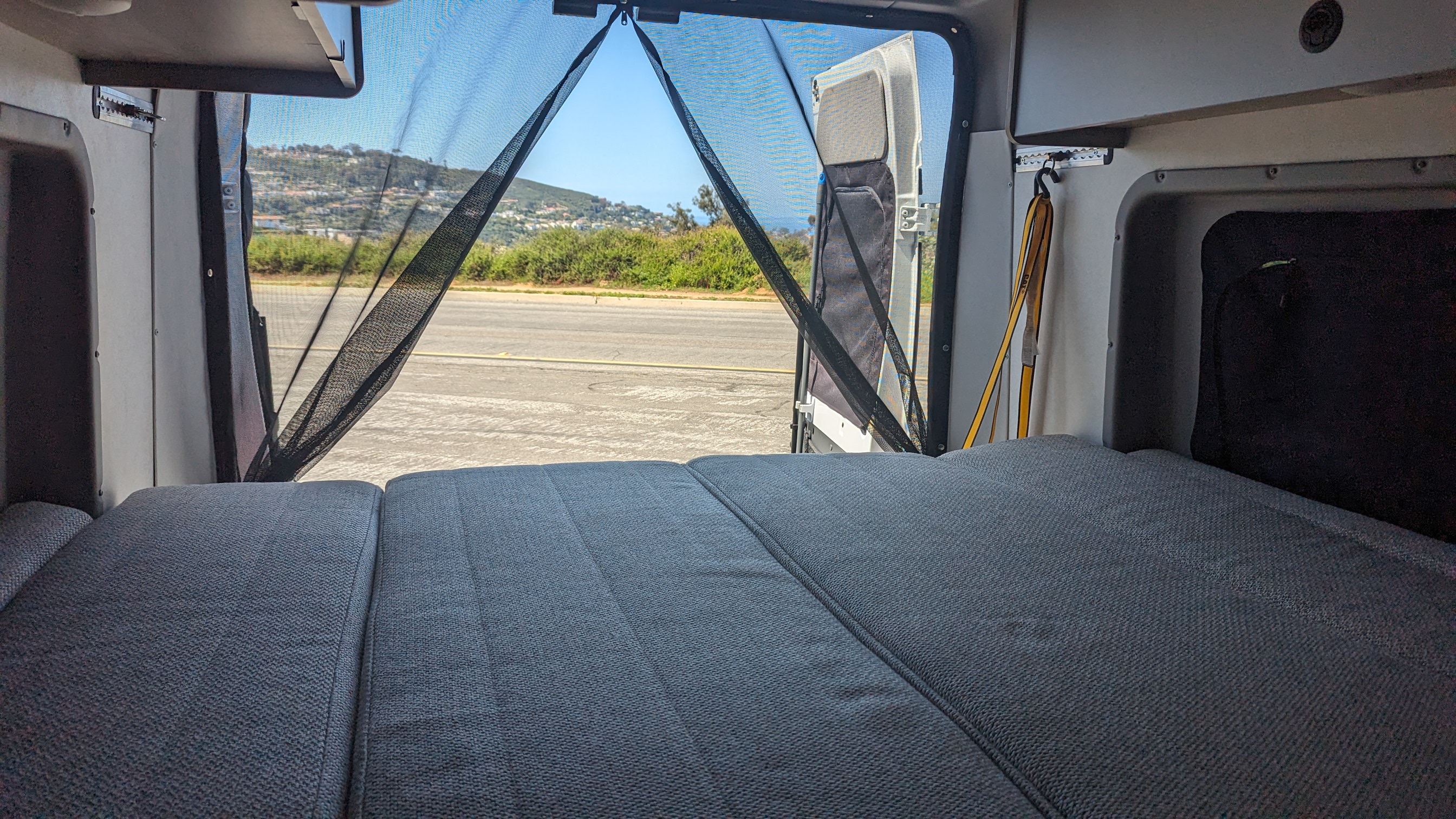 Inside a spacious RV rental, a comfortable bed faces open rear doors with a mesh screen & scenic outdoor view.. Winnebago Solis 59PX 2023