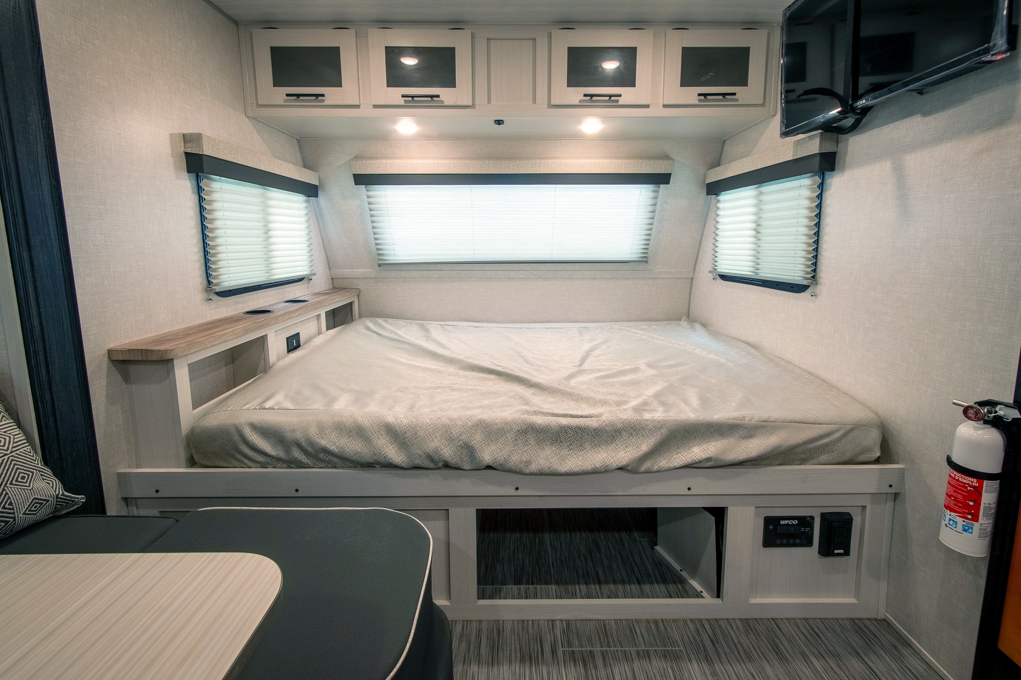 Cozy RV rental bedroom featuring a queen bed, overhead storage, side windows, TV, and convenient bedside shelf with outlets.. No Boundaries 19.8 2024