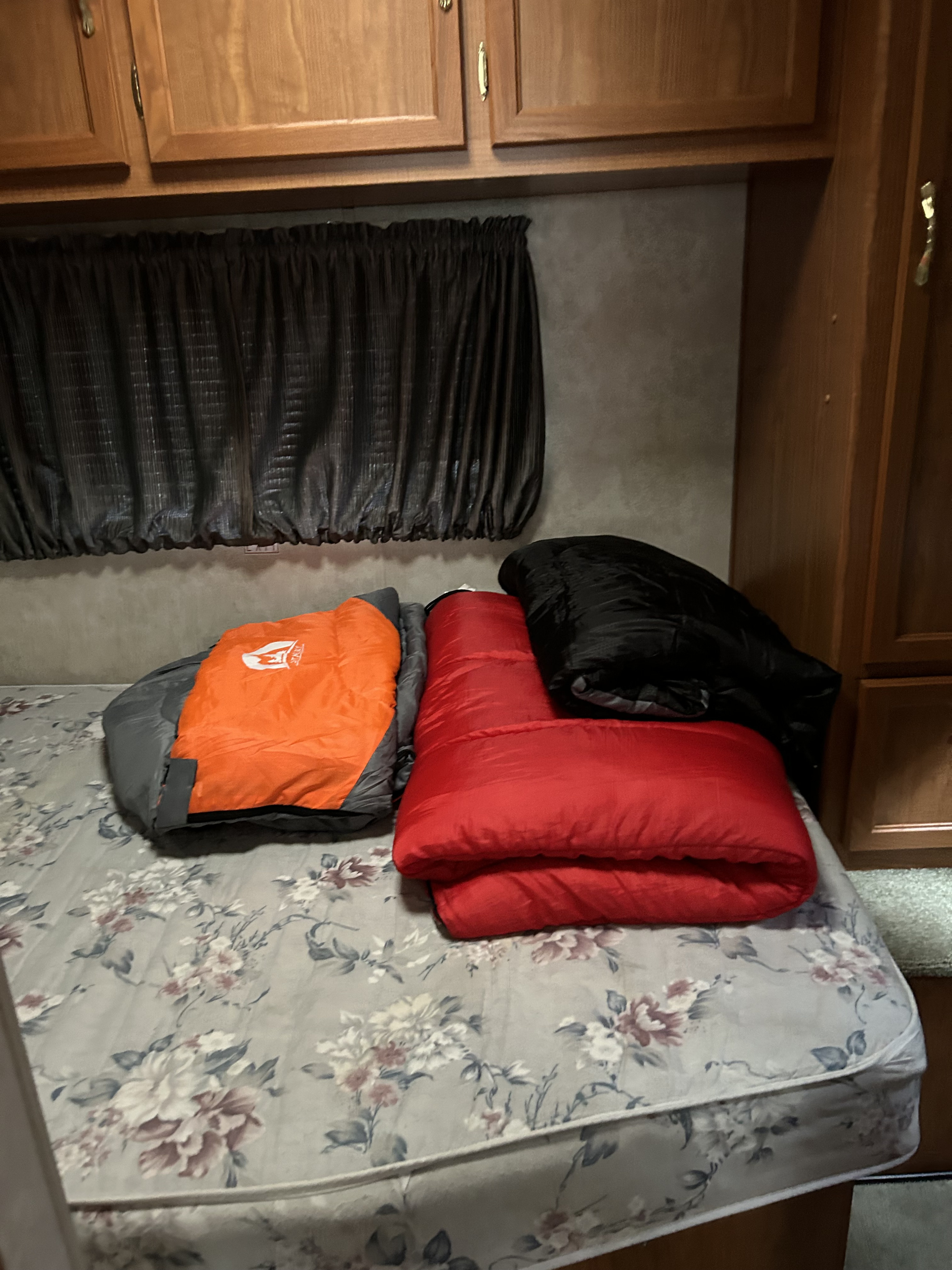 An RV rental bedroom with three colorful sleeping bags (orange, red, black) on a floral mattress.. Coachmen Catalina 2003