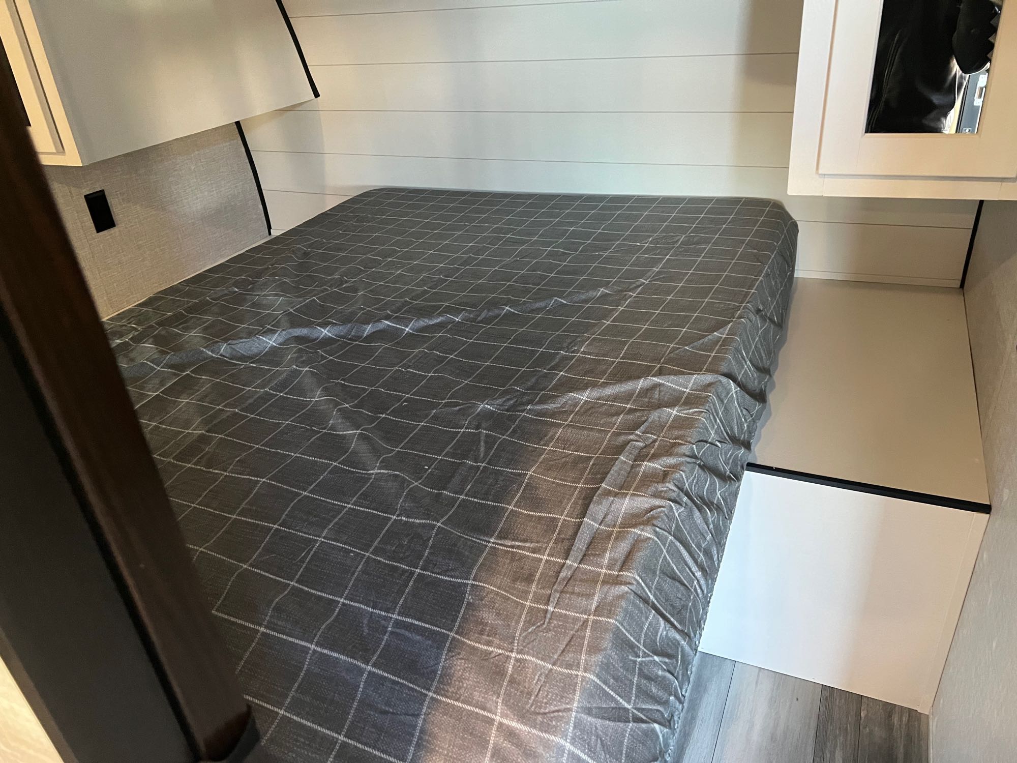 Cozy RV rental bedroom featuring a plaid-covered bed, white shiplap walls, and compact storage with a mirror.. Jayco Jayflight 2024