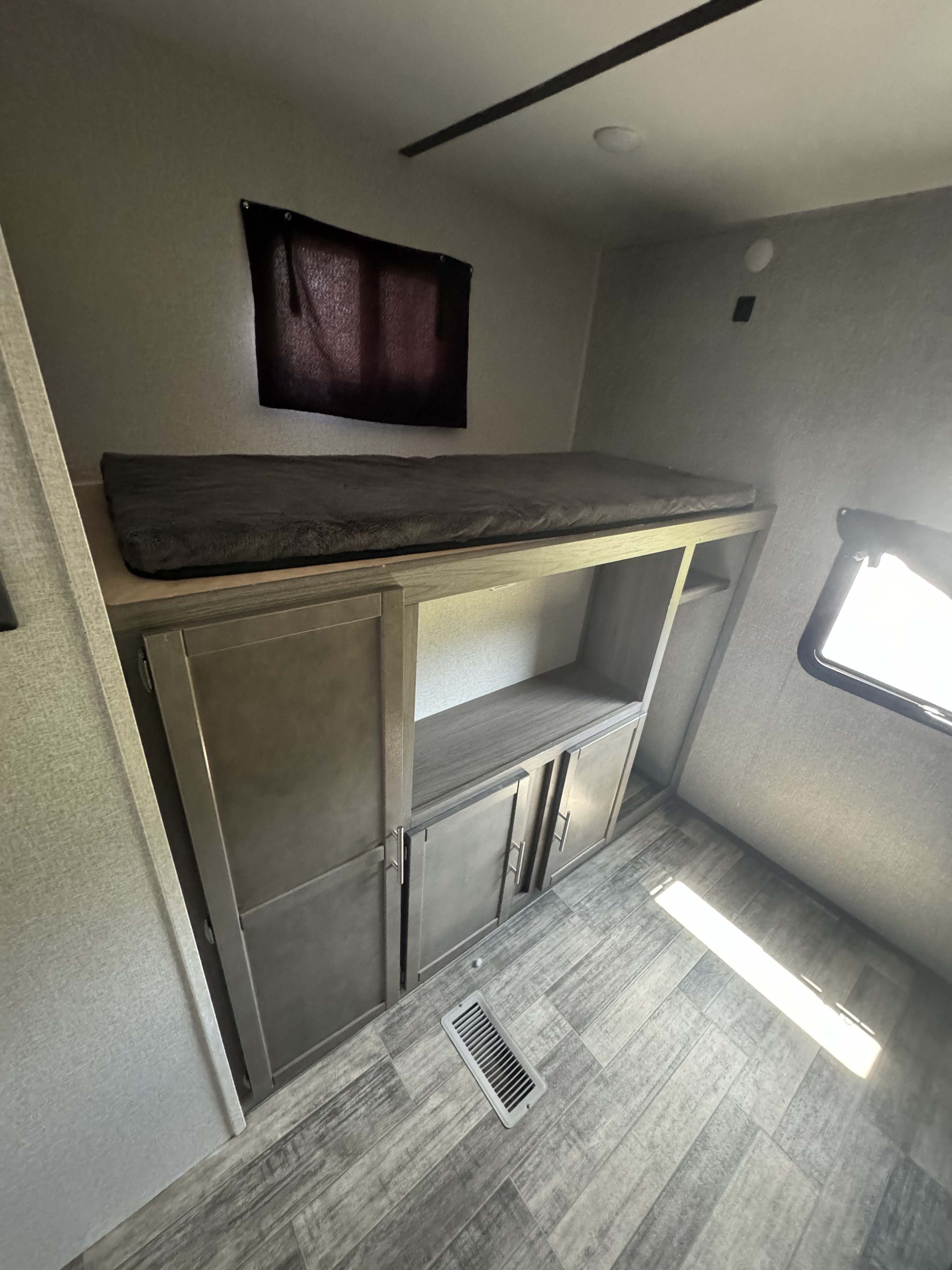 RV rental interior: A comfortable bunk bed over storage cabinets and shelves, with a window and wood-patterned floor.. Crossroads Volante 2021